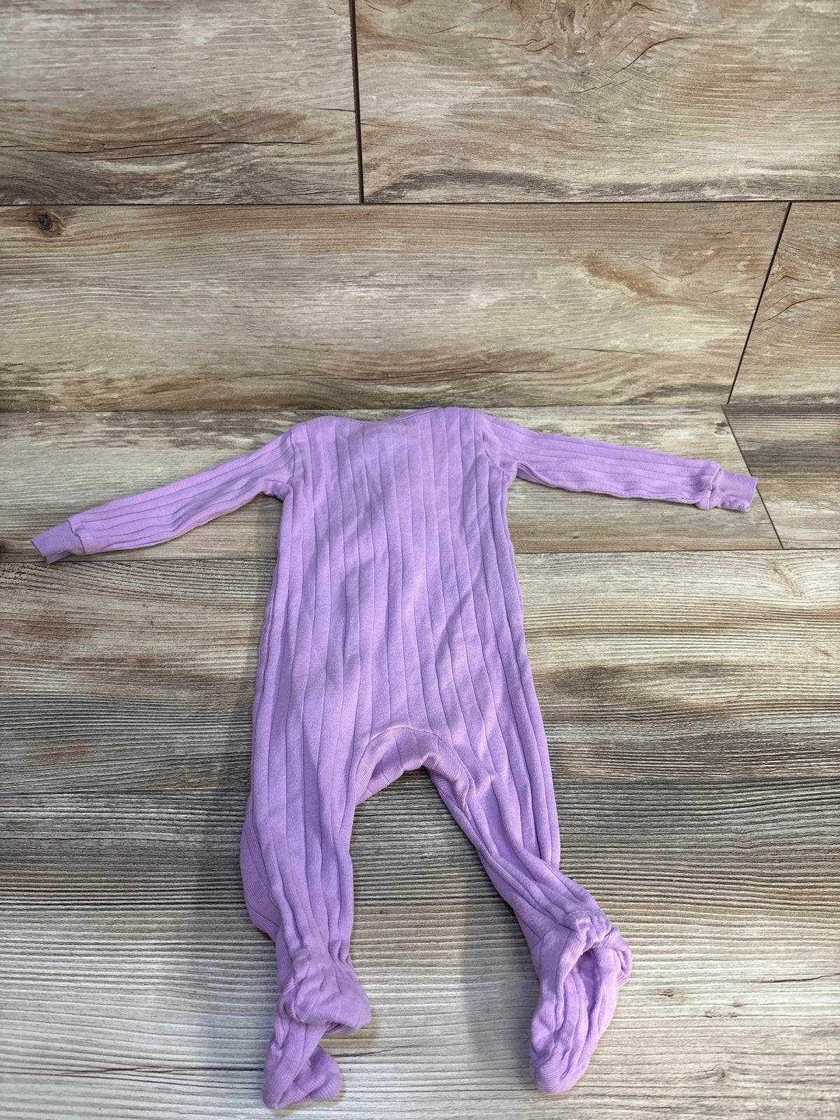 Laid flat view of Member’s Mark purple ribbed sleeper showcasing long sleeves and footed legs on a wood floor