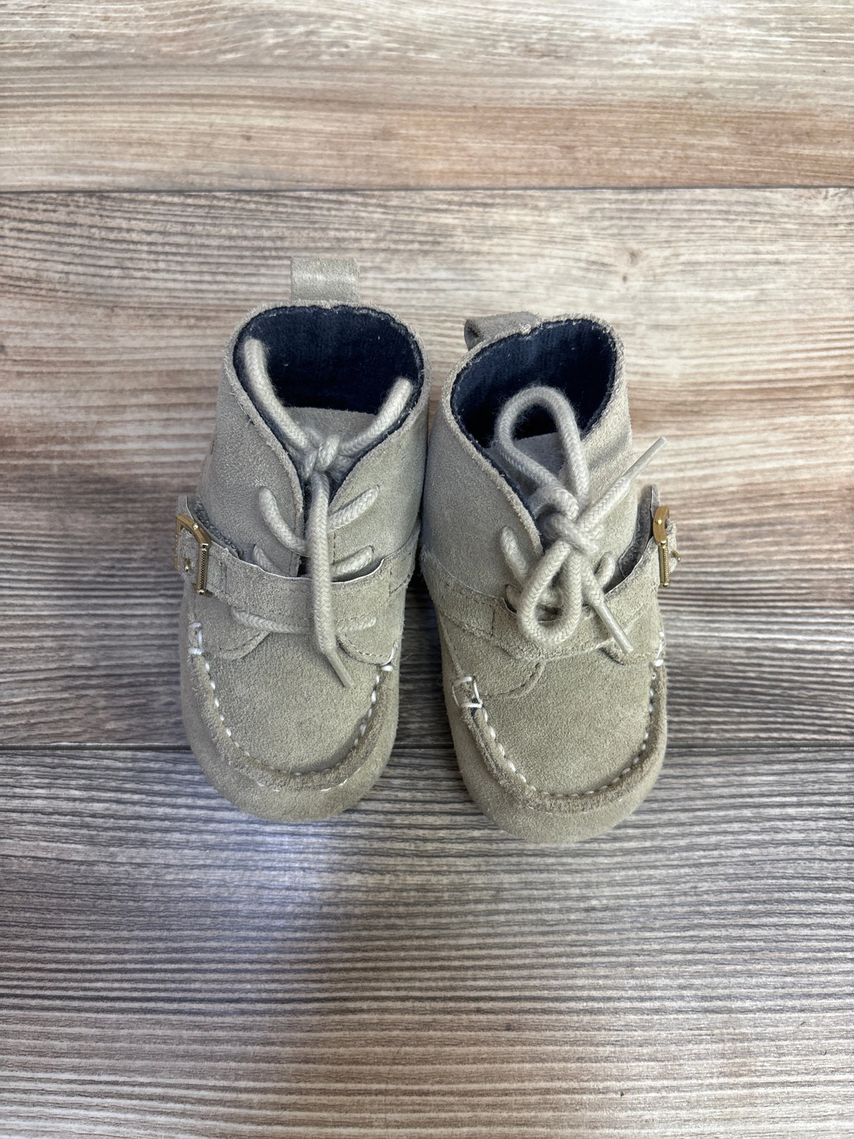 Pair of light gray suede baby shoes with laces and strap on wood surface