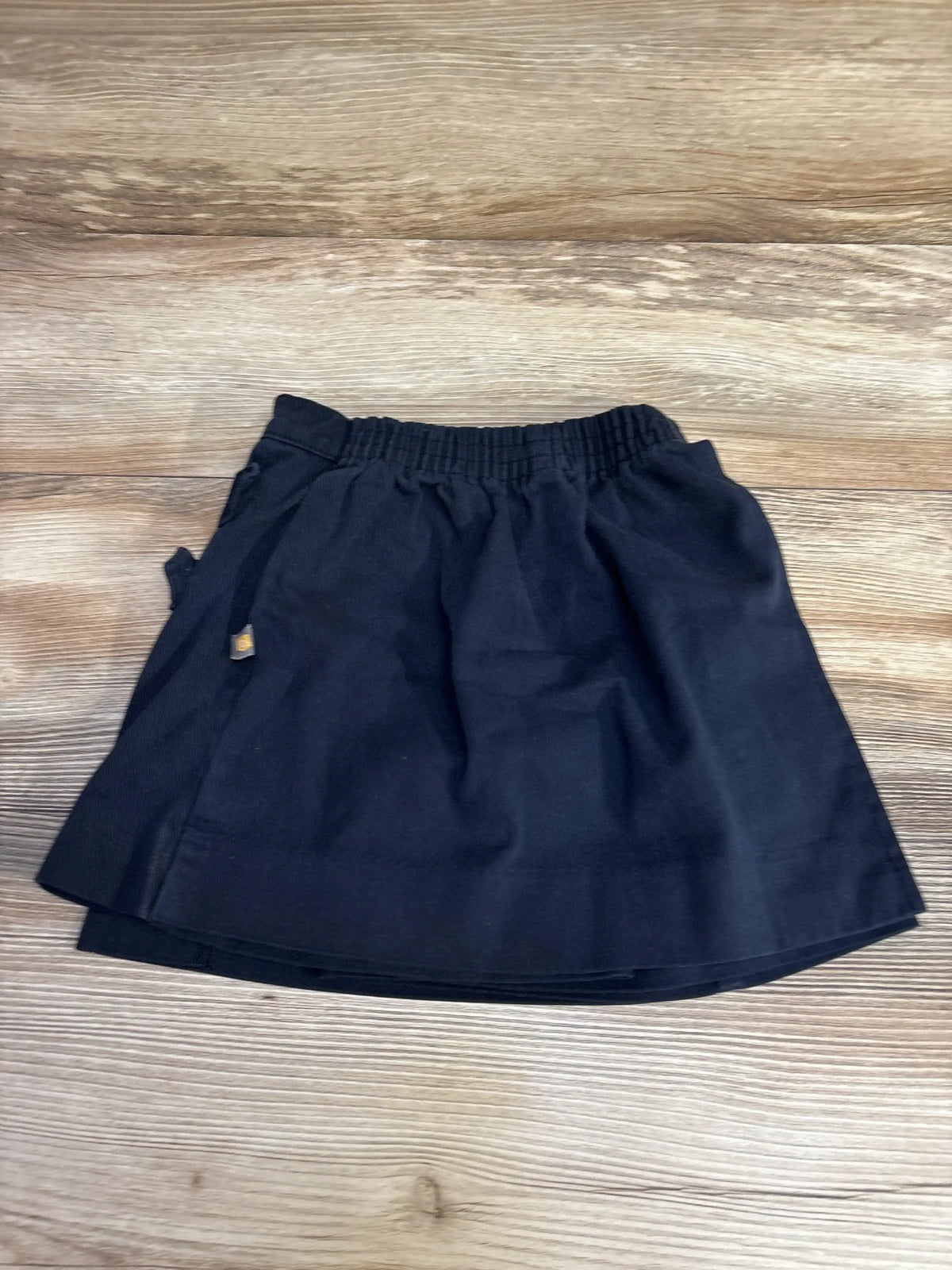 Flat lay of navy girls' Dennis school skort, size 4, showing elastic waistband and front panel on wood floor