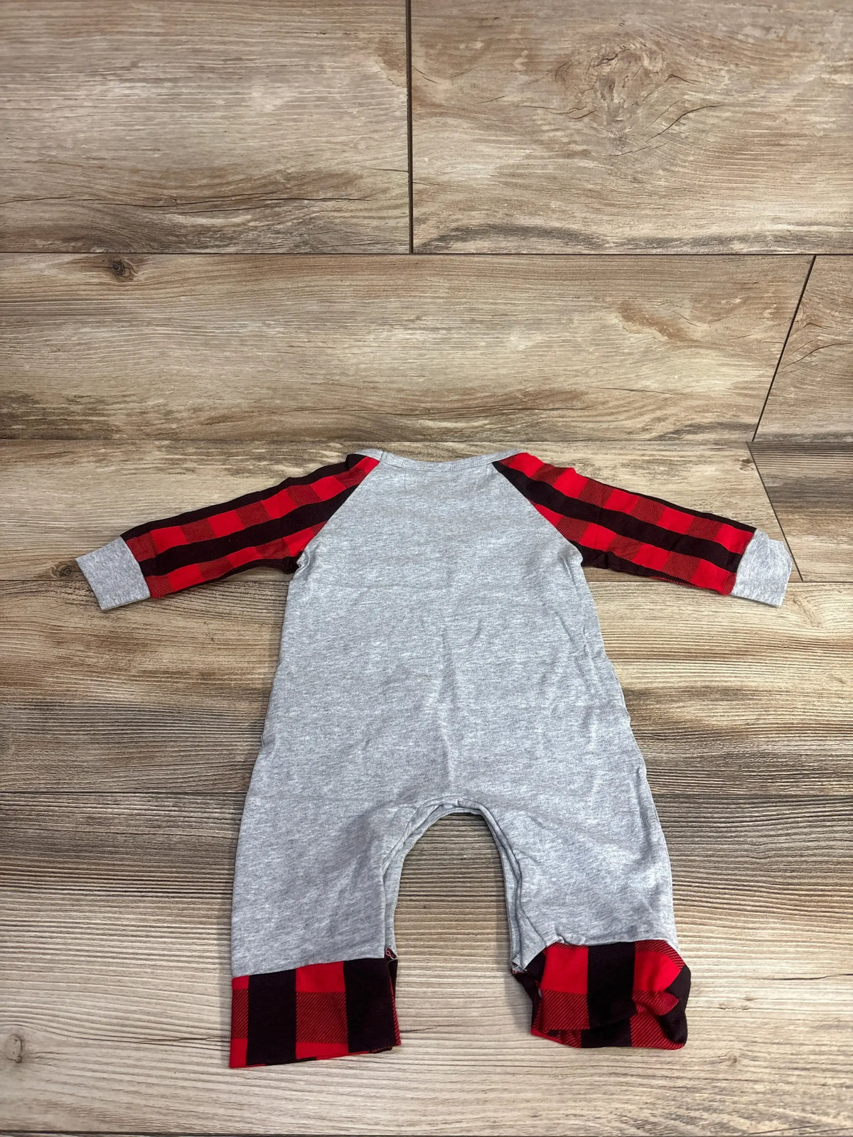 Gray baby onesie with red and black buffalo plaid sleeves and cuffs, laid on wood floor
