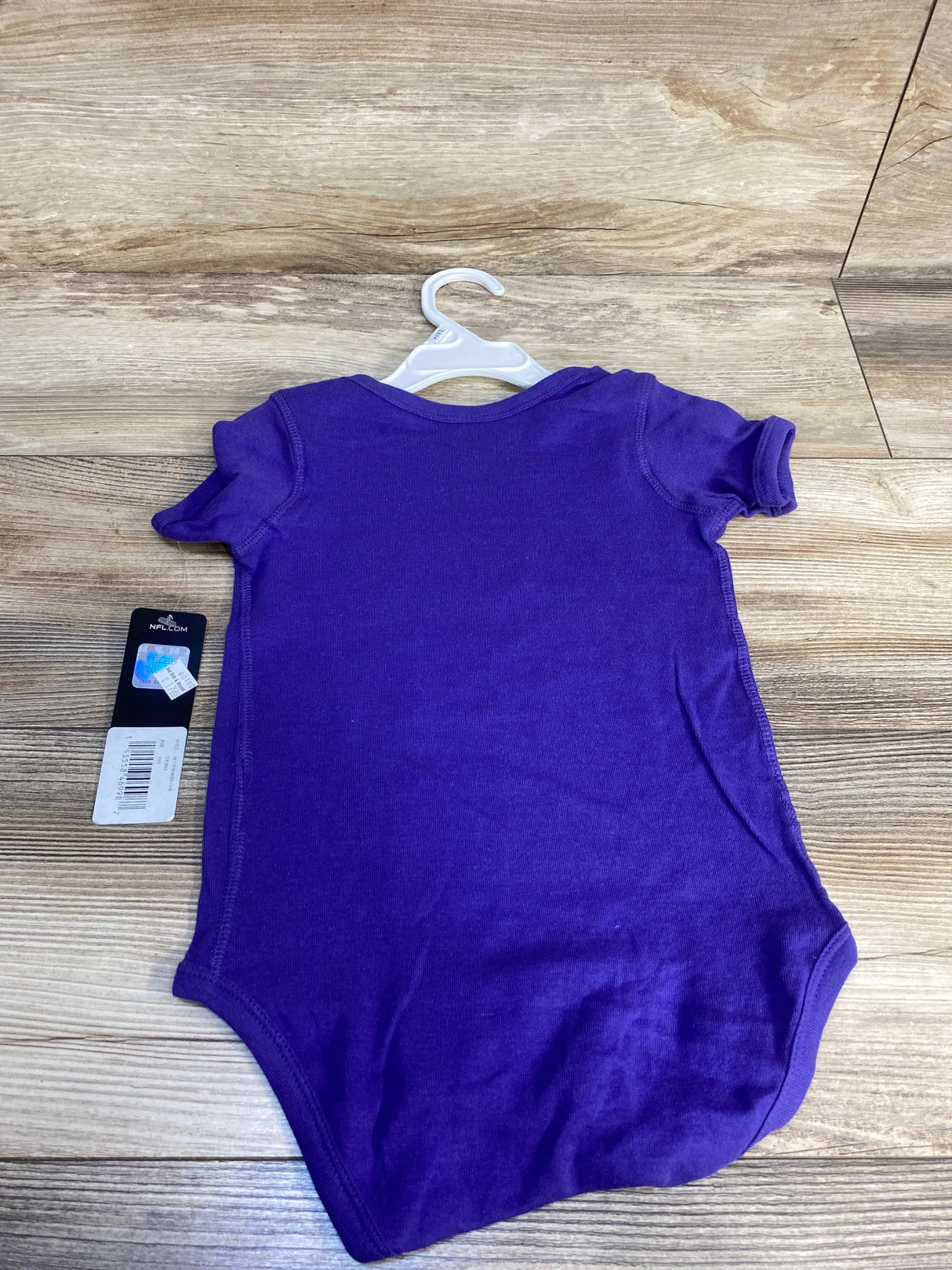 Purple short sleeve baby bodysuit on hanger, new with tag, on wooden background