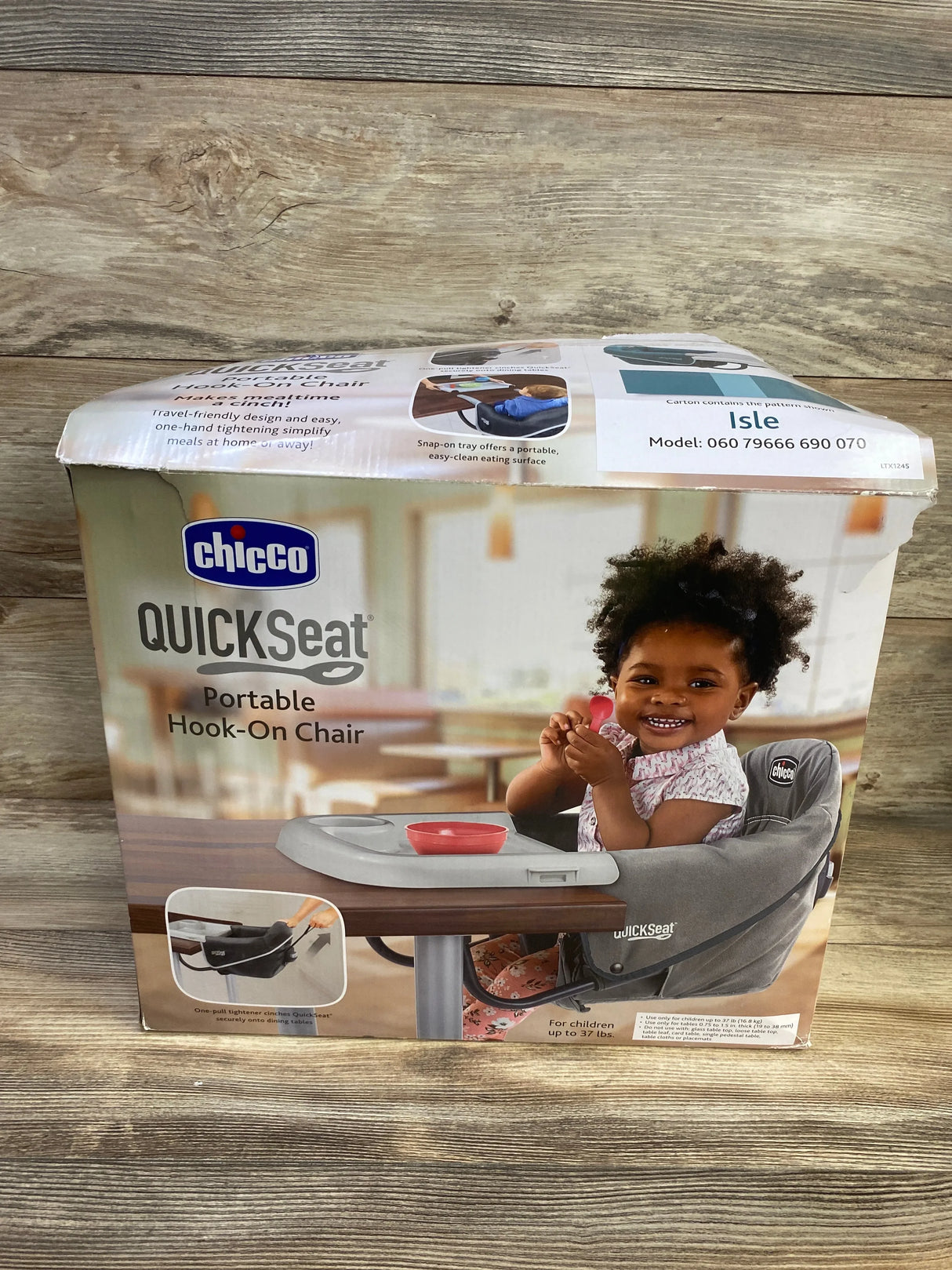 Front view of Chicco QuickSeat portable hook-on chair box showing gray seat with tray and smiling toddler on wooden tabletop