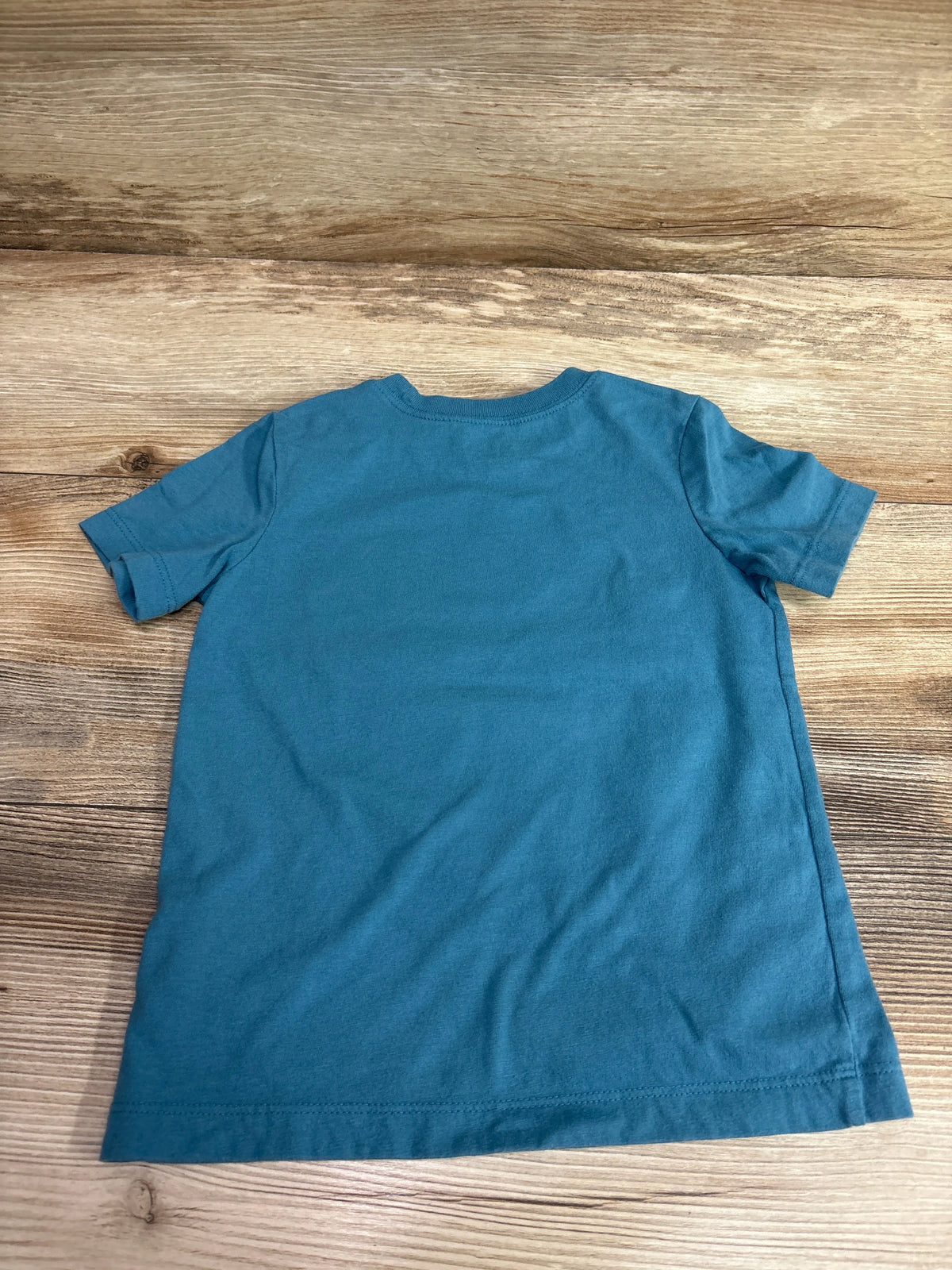 Front view of Oshkosh blue shirt in size 3T showcasing short sleeves and crew neck with a wood-grain background