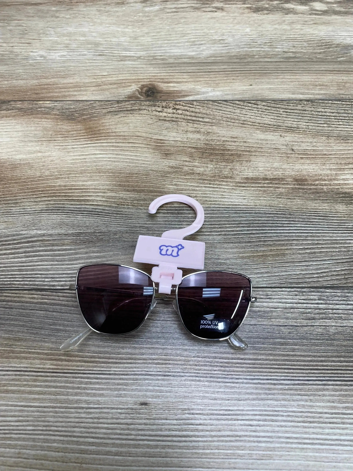 Front view of More Than Magic sunglasses with silver frame, purple lenses and 100 percent UV protection on wood