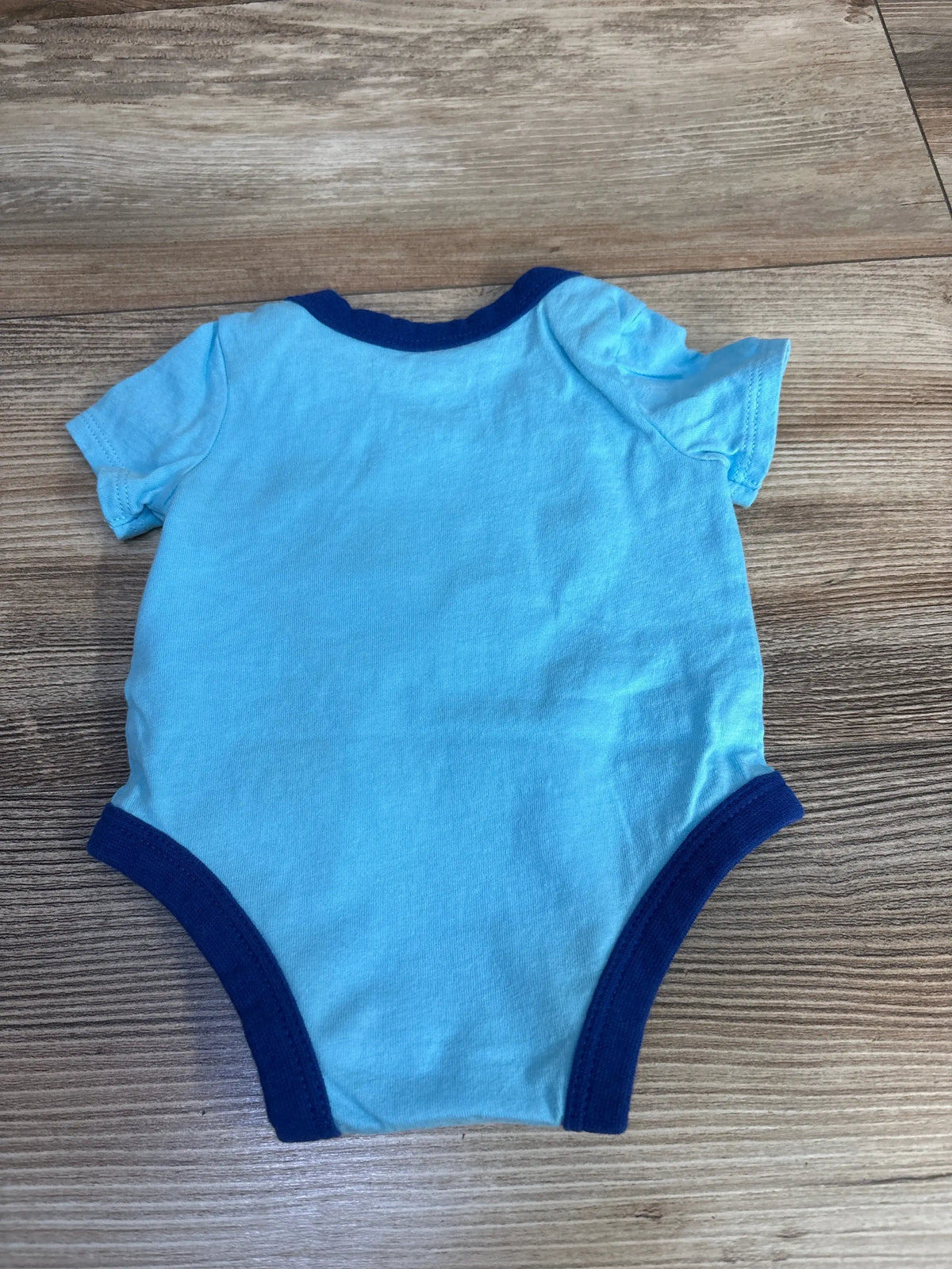 Back view of newborn blue Nike bodysuit showcasing navy trim and short sleeves on wooden floor background