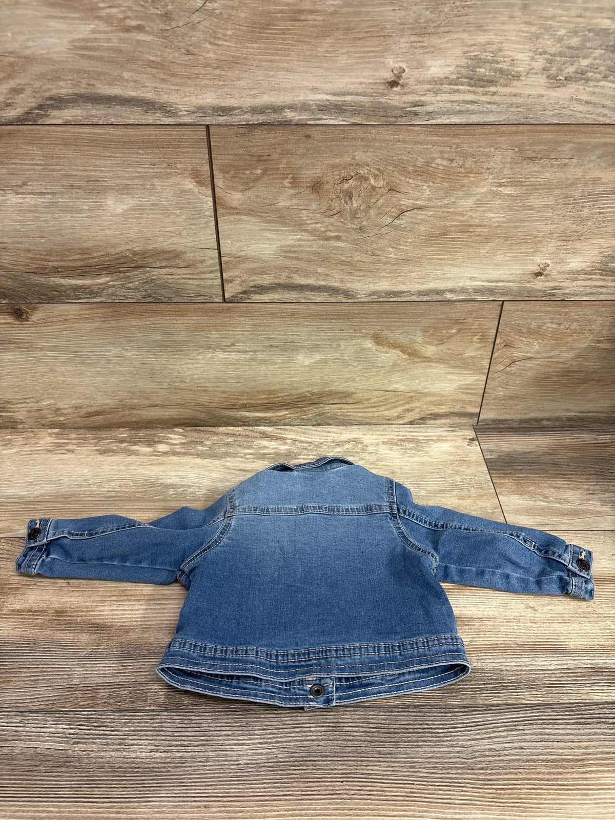 Back view of Okie Dokie blue denim jacket size 9m showcasing long sleeves and button closures on wood plank background