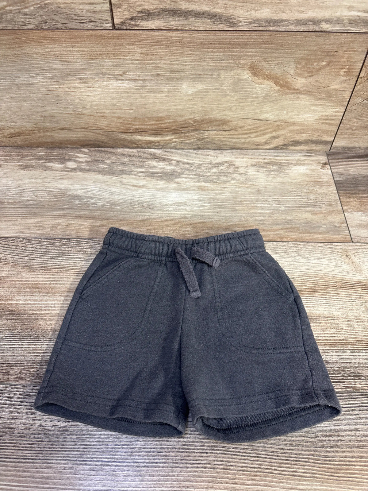 Top down view of grey knit toddler shorts with elastic drawstring waistband and front pockets on wood background
