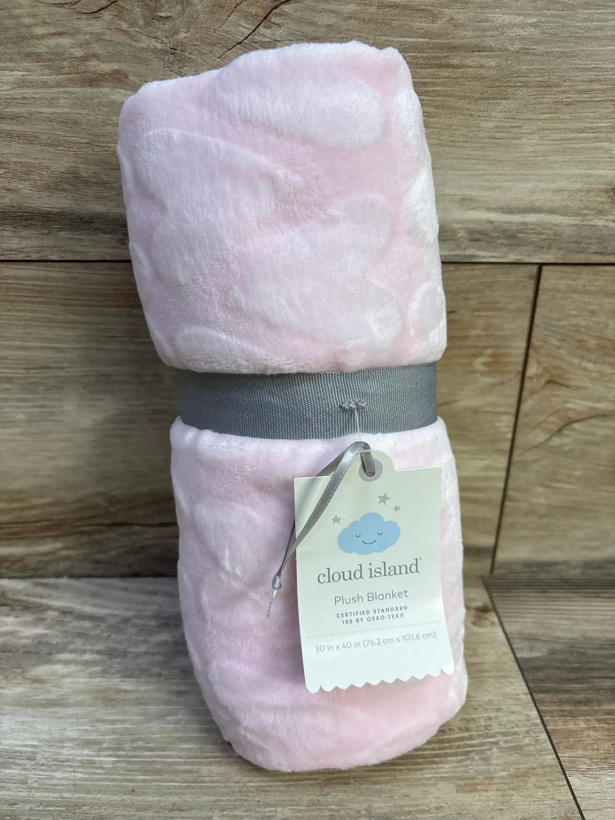Rolled pink Cloud Island plush baby blanket with embossed hearts, gray ribbon and tag on wood background