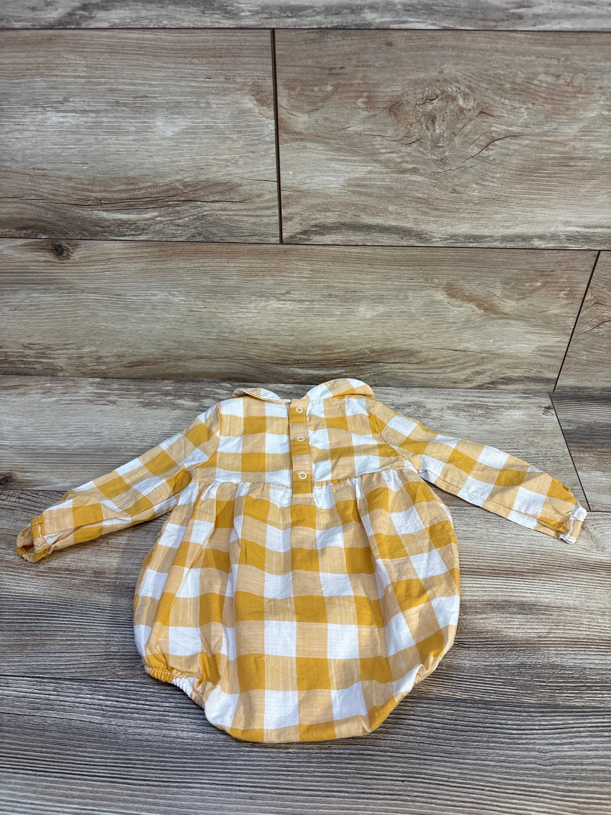 Yellow and white gingham baby romper with long sleeves, laid on wood floor
