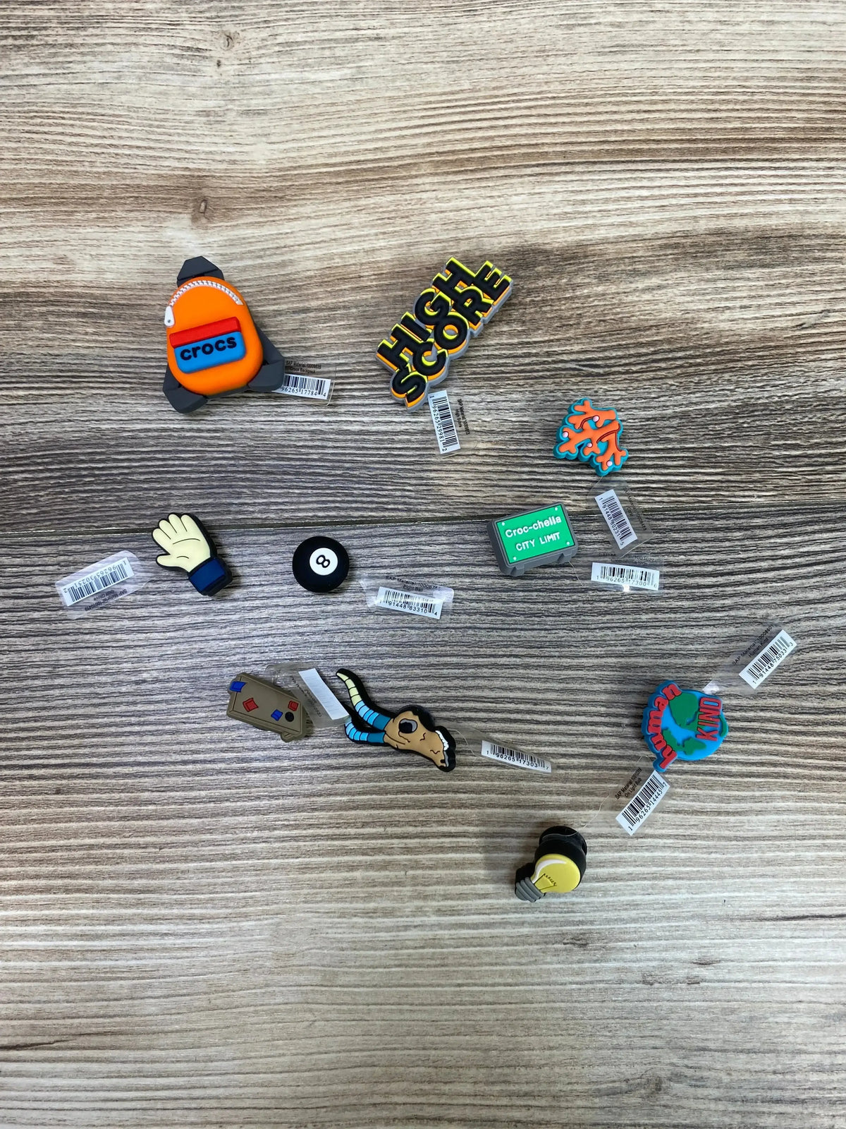 Top view of 10 Croc Jibbitz charms showcasing assorted colorful designs on a wood-grain surface