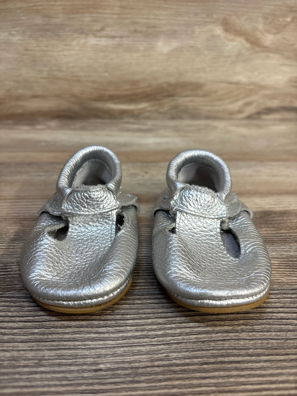 Silver baby moccasins with soft soles on wooden background