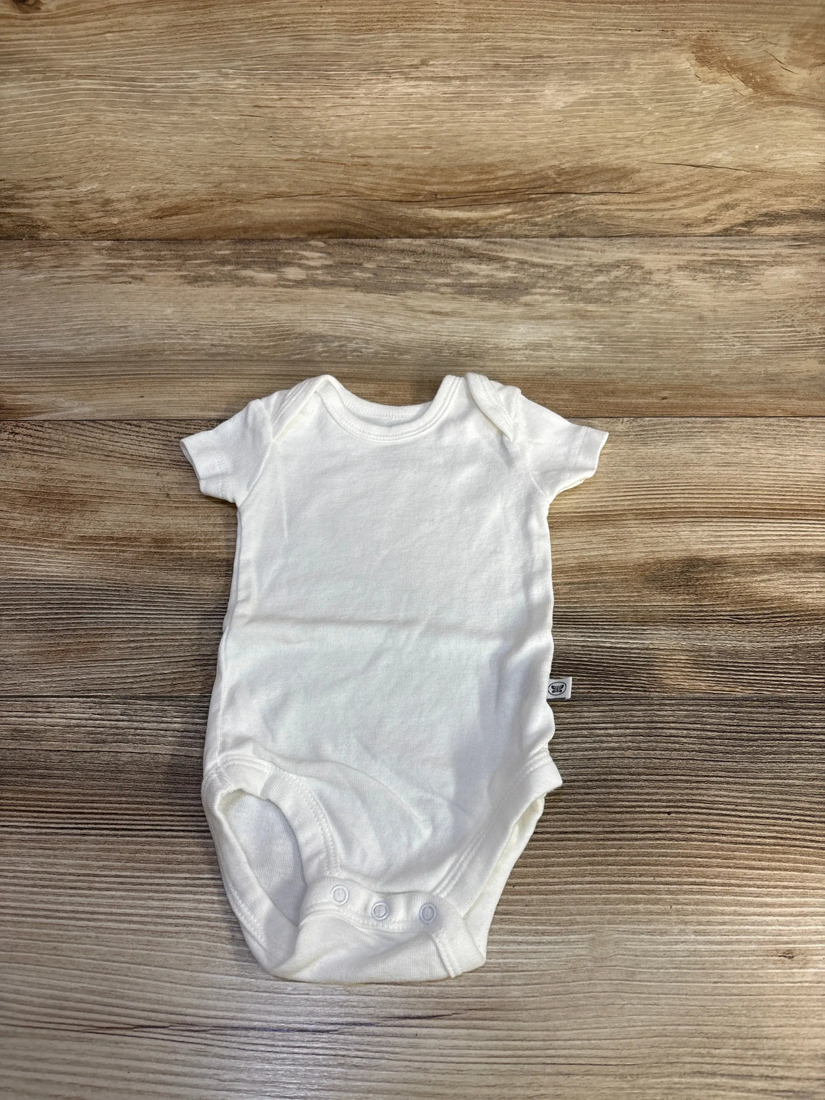 Front view of Honest Baby white bodysuit in size 0 to 3 months showcasing short sleeves and three snap closures on a wood grain background