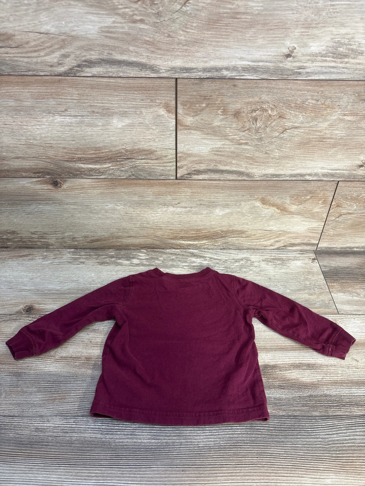 Back view of Carter’s hot dog shirt showing plain maroon fabric and long sleeves on a wood-look floor
