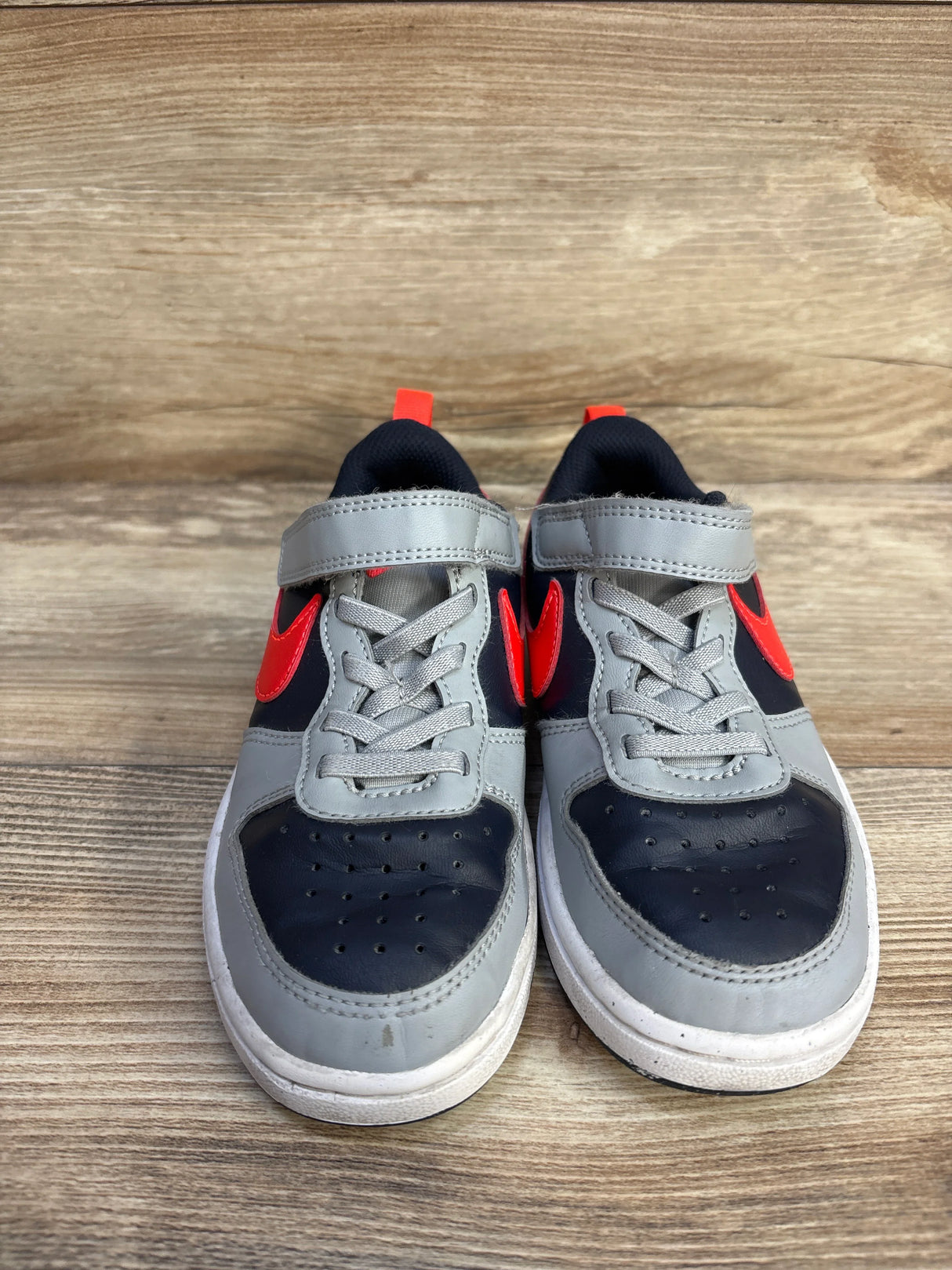 Gray and black kids sneakers with orange swoosh on wooden floor