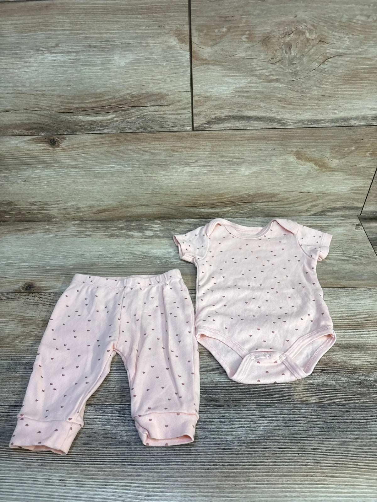 Pink baby onesie and pants set with heart print, soft newborn clothing on wood floor