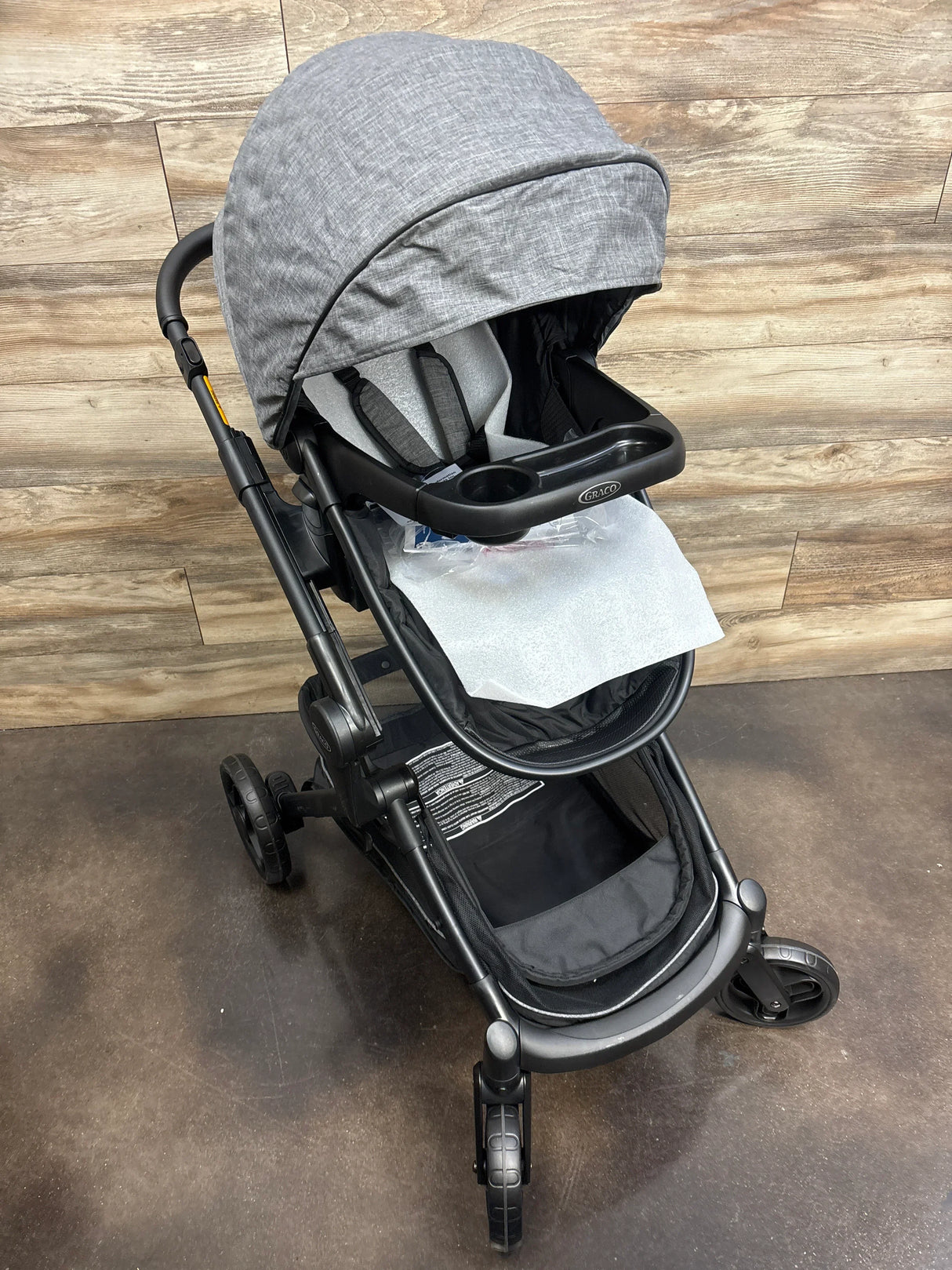 Gray Graco baby stroller with canopy and tray on a wood and concrete floor background