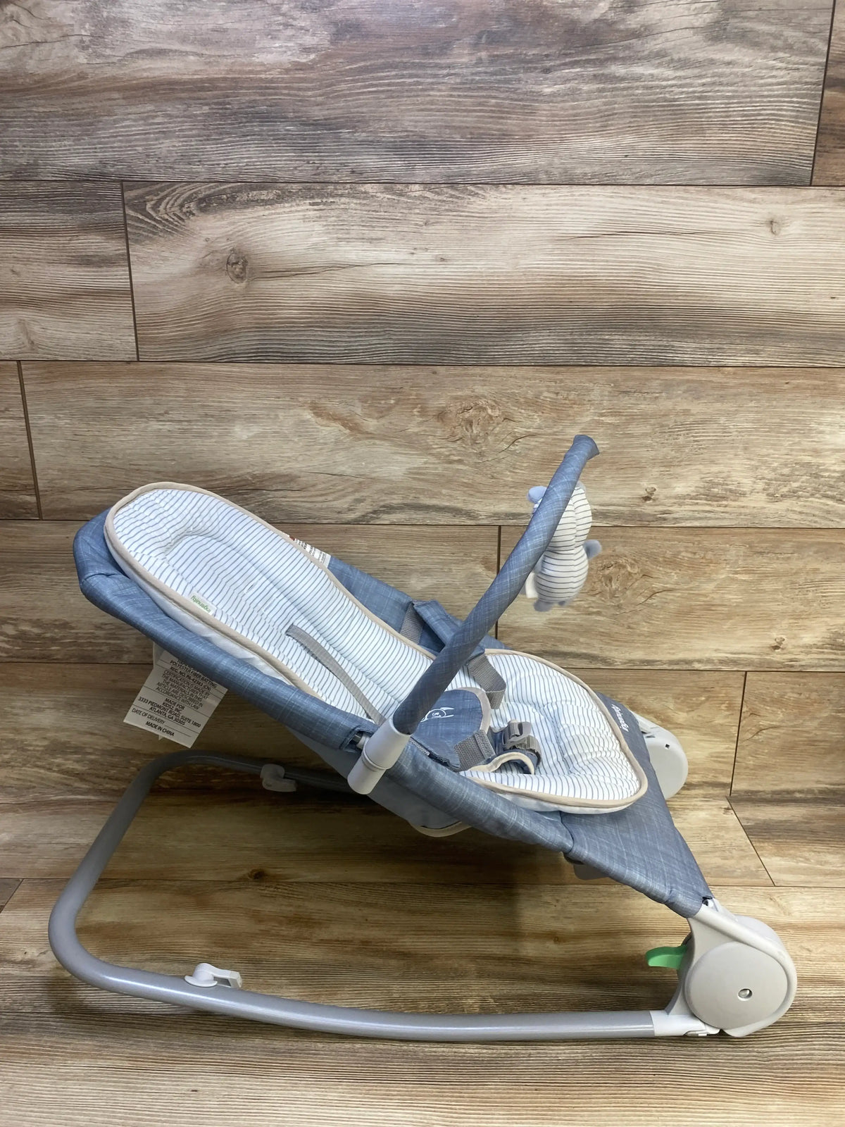 Side view of Ingenuity 2-in-1 Happy Belly rock-to-bounce baby seat with striped liner, harness and toy bar on wood floor