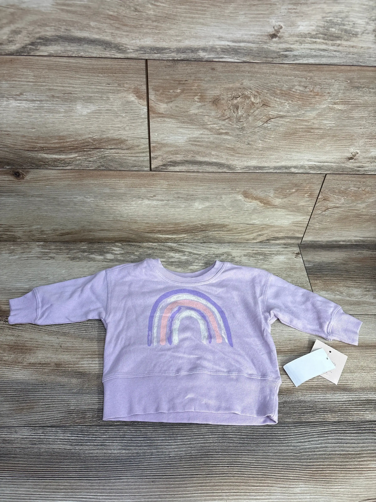 Lavender toddler sweatshirt with pastel rainbow print and ribbed cuffs on wooden floor