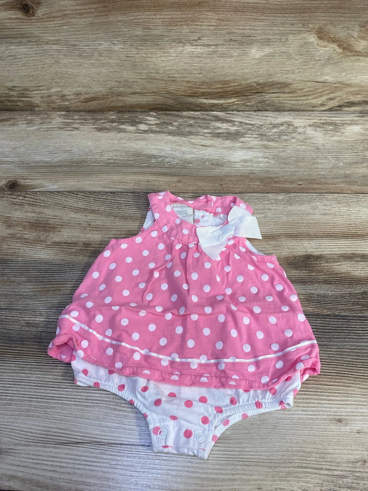 Front view of pink polka dot bow bodysuit dress showcasing white bow and sleeveless design on wood background