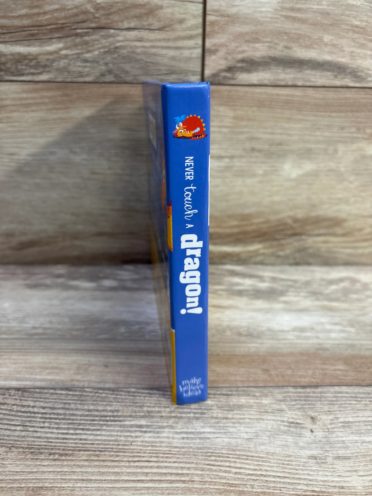Side view of Never Touch a Dragon board book spine showing title and dragon illustration on wood background
