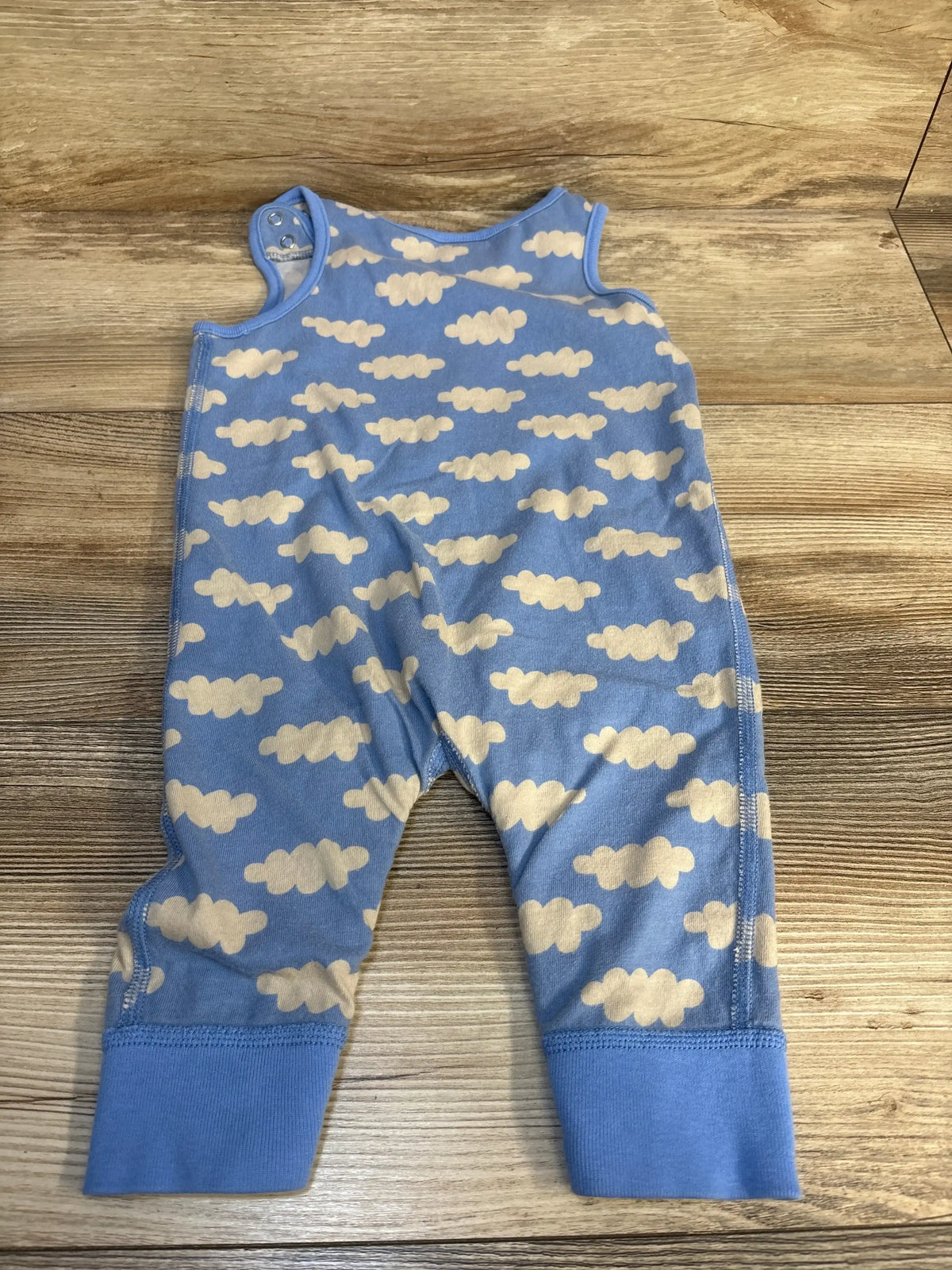 Blue baby romper with white cloud print, snap shoulder, laid flat on wooden surface