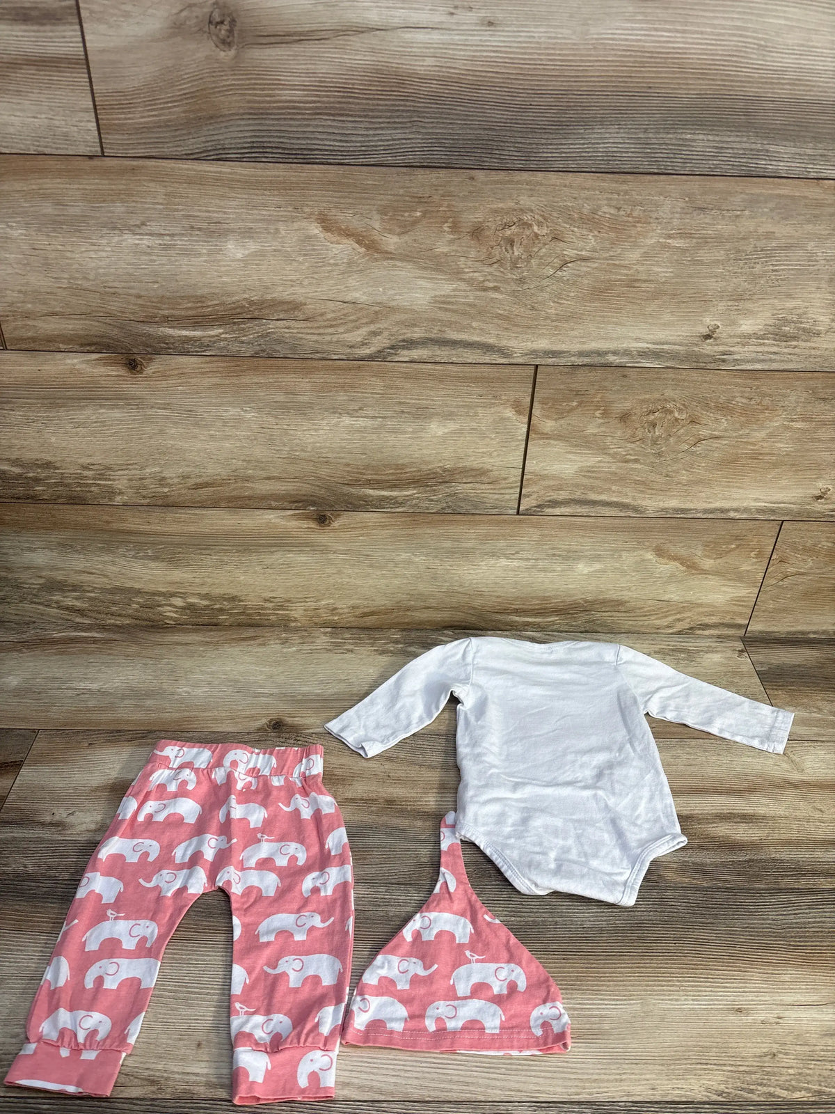 Top down view of PatPat three piece baby set showcasing white bodysuit and pink elephant print pants and hat on wood flooring