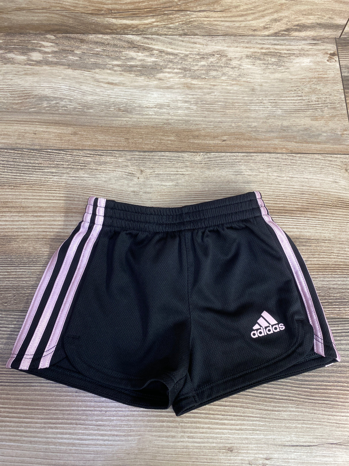 Black Adidas athletic shorts with pink three stripes and logo on wooden floor