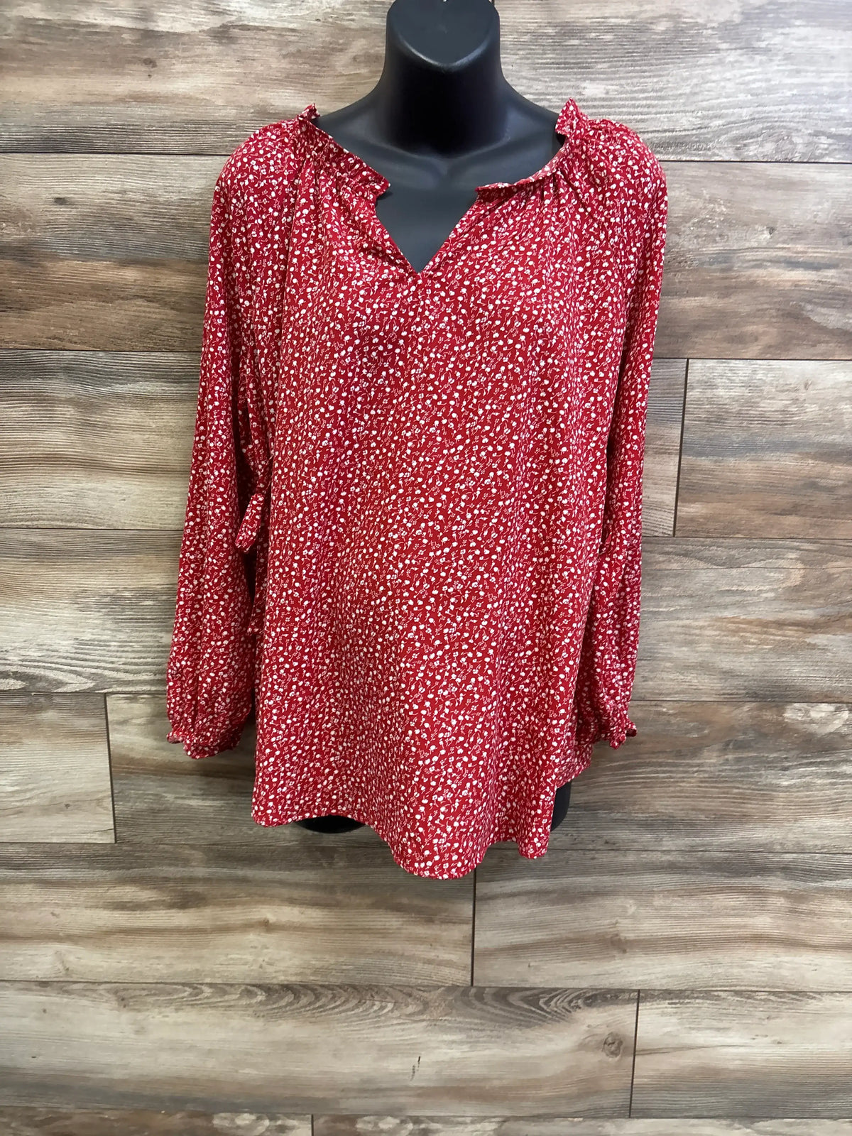 Front view of Isabel maternity red ditsy floral long-sleeve top showing ruffled V-neck and gathered cuffs on wood-plank backdrop