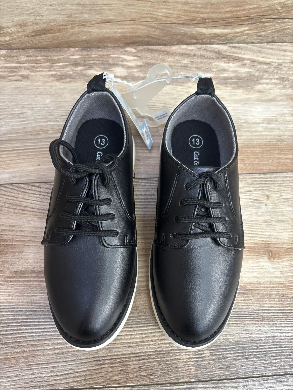 Overhead view of Cat & Jack Alfi toddler black dress shoes showing laces, white soles, size 13 on wooden floor