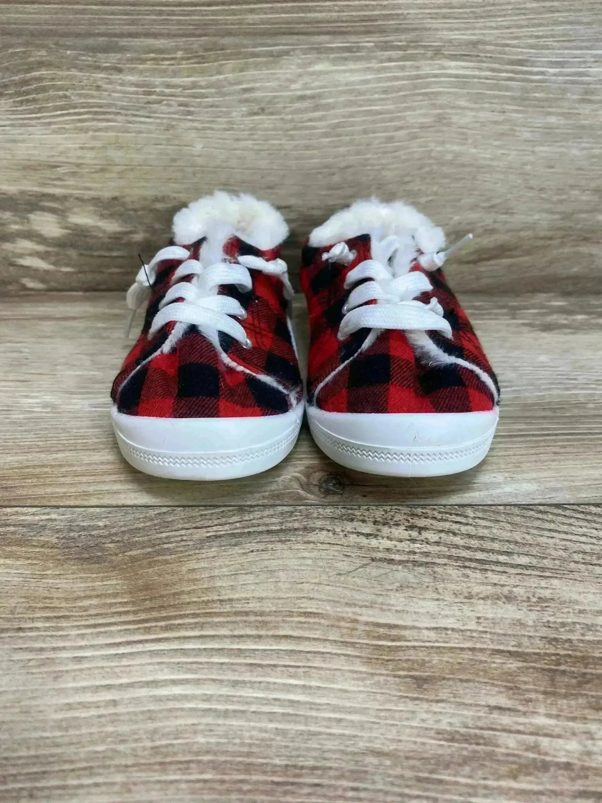 Front view of toddler slip-on sneakers in red and black buffalo plaid with faux fur lining on a wood floor