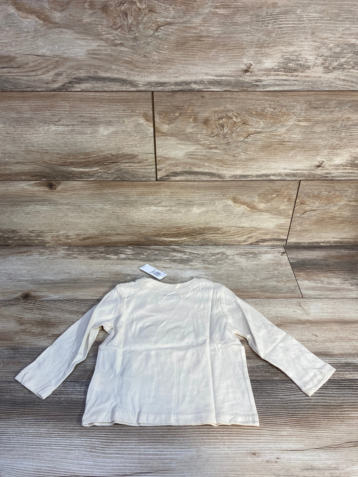 Cream long sleeve baby shirt on wood background with tag attached