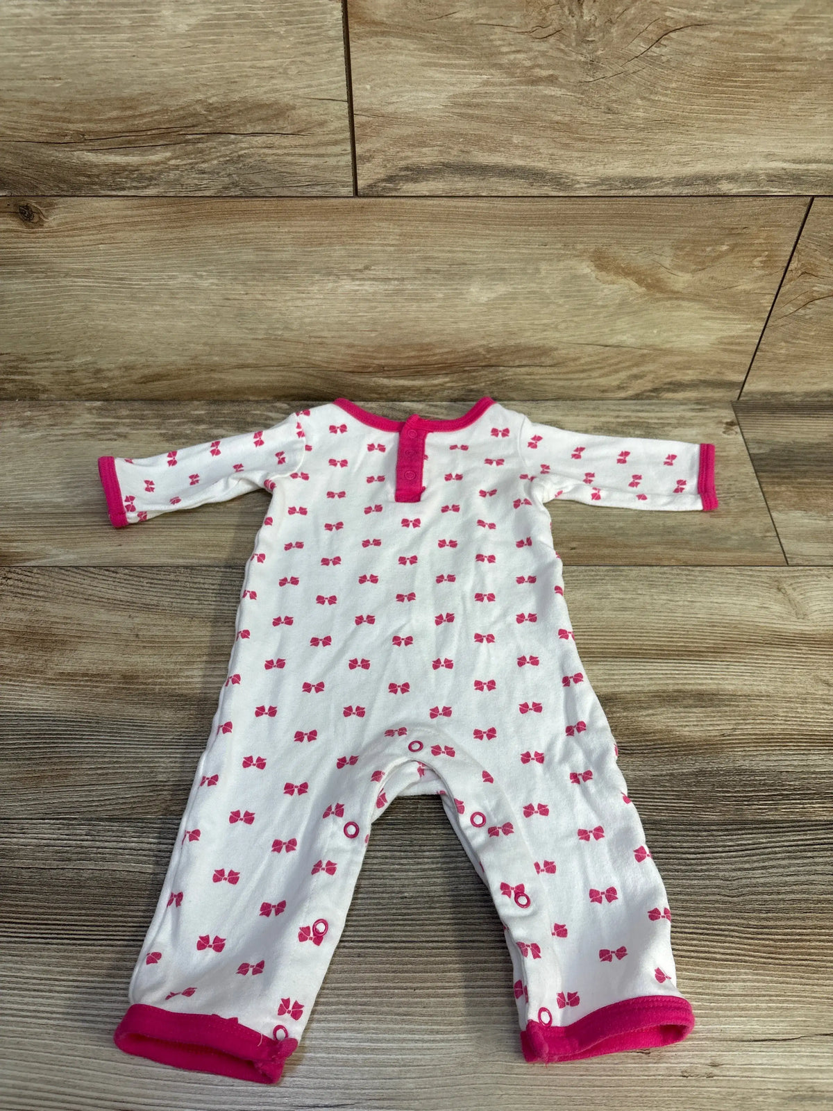 Front view of Hudson Baby white bow print coverall showcasing henley neckline and snap closures on wood flooring