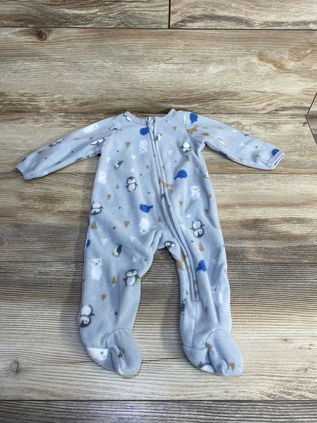 Flat-lay of grey fleece footed baby sleeper (3–6M) with penguin and bear print and zipper on light wood background