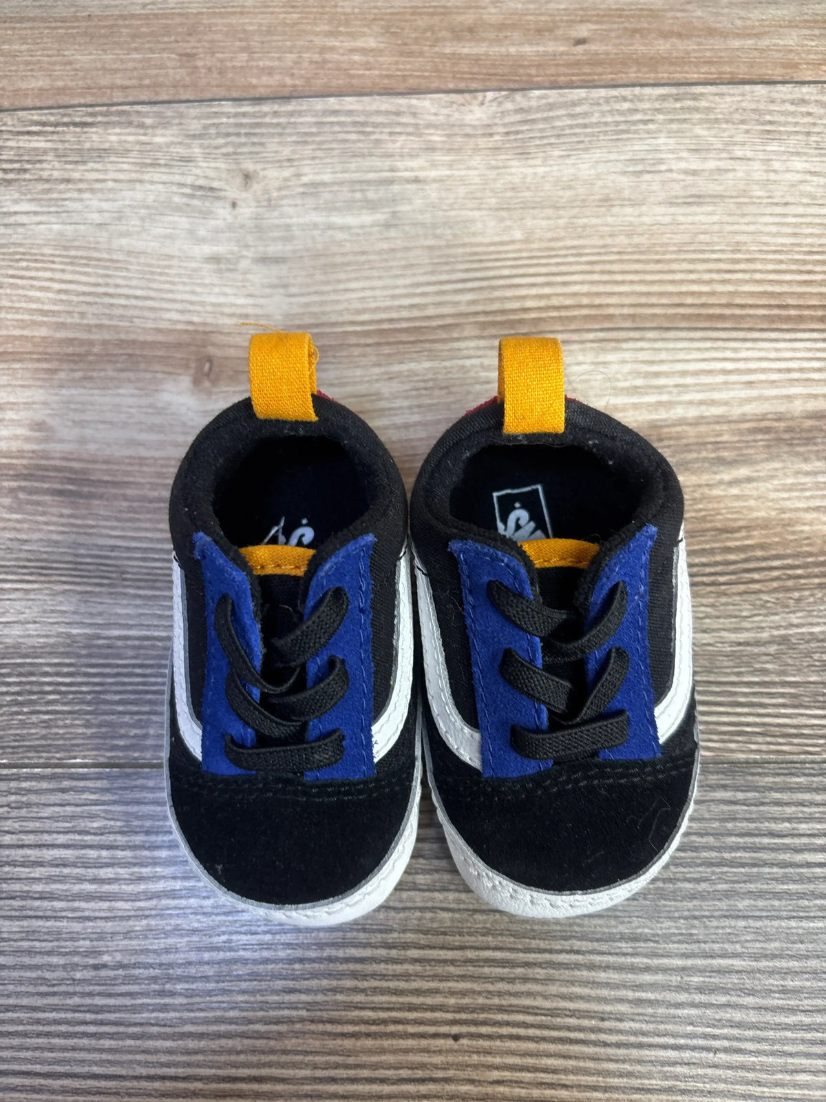 Front view of black Vans Old Skool Crib Shoes with canvas and suede textile uppers, white side stripes, and yellow heel pull tabs