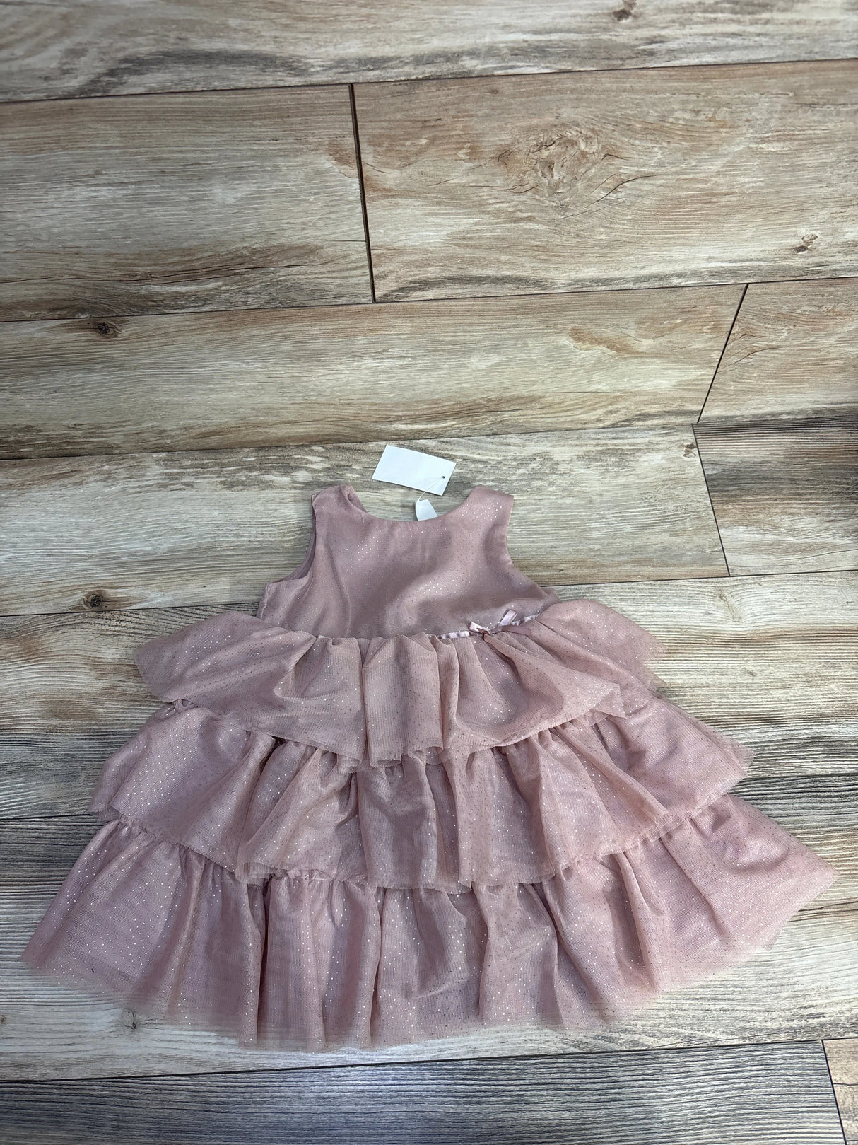 Pink sleeveless baby dress with sparkly layered tulle skirt on wooden floor