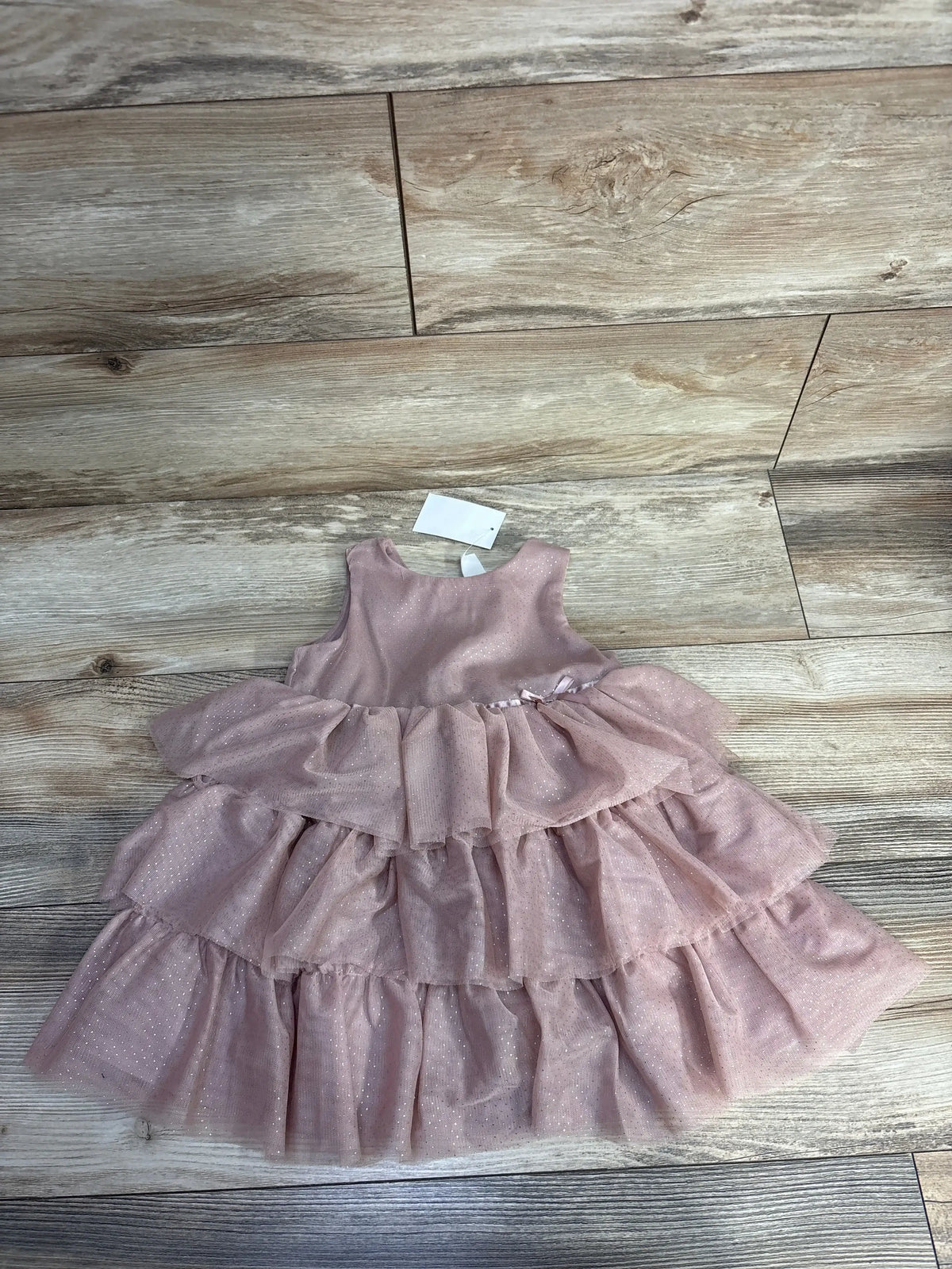 Pink sleeveless baby dress with sparkly layered tulle skirt on wooden floor