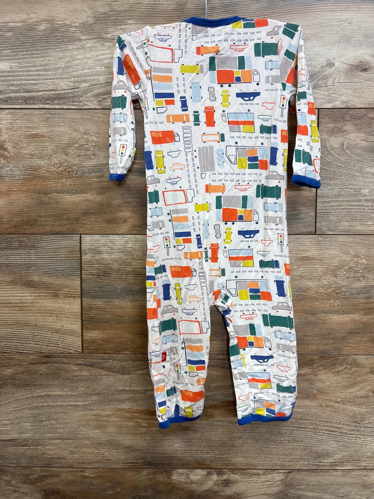 Back view of Magnetic Me Modal footed baby pajama in white showcasing colorful traffic and truck print with blue cuffs on wood background