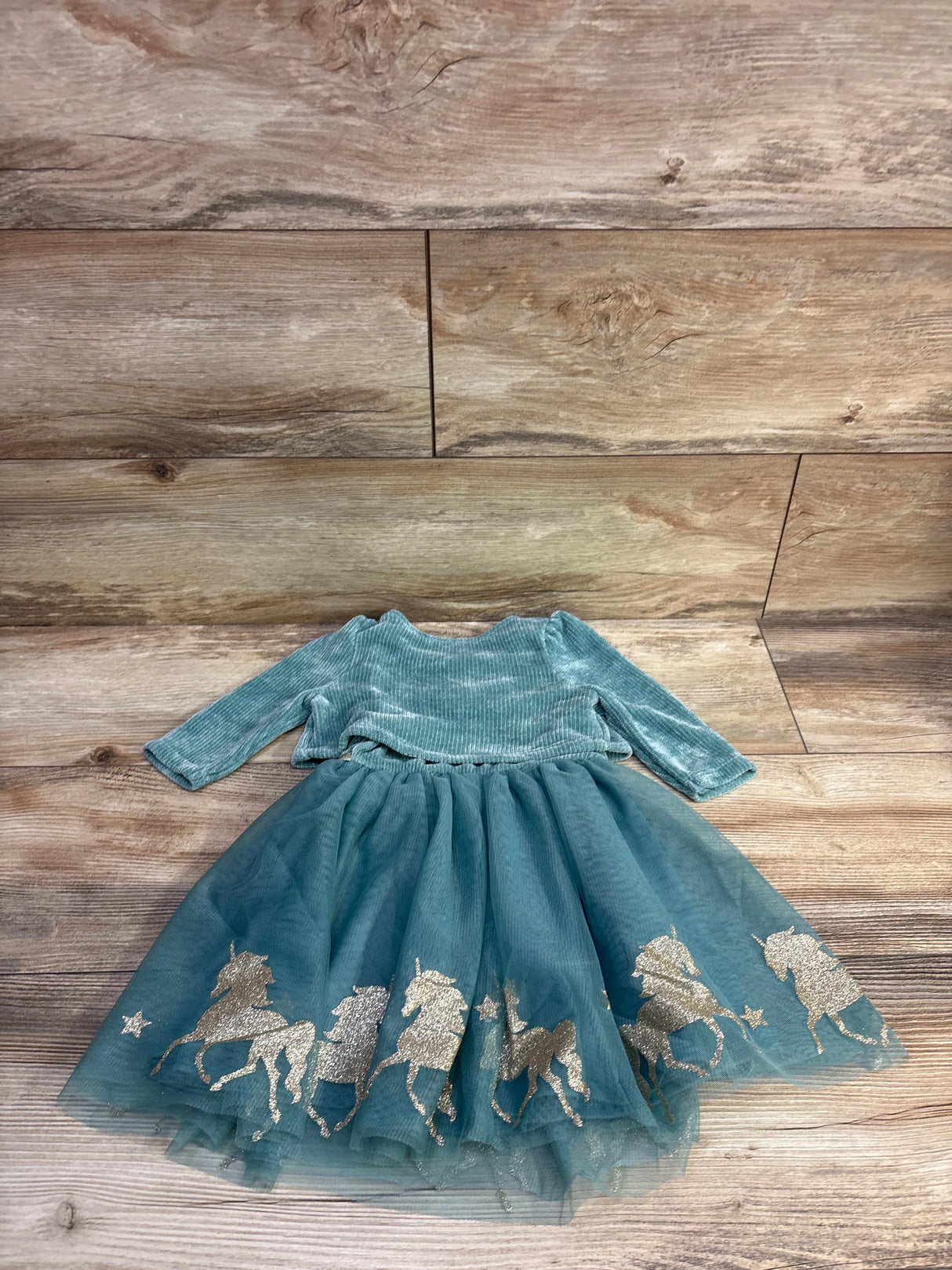 Flat lay of 2-piece velvet tulle dress and cardigan set showcasing gold-glitter unicorn border on teal tulle with wood background