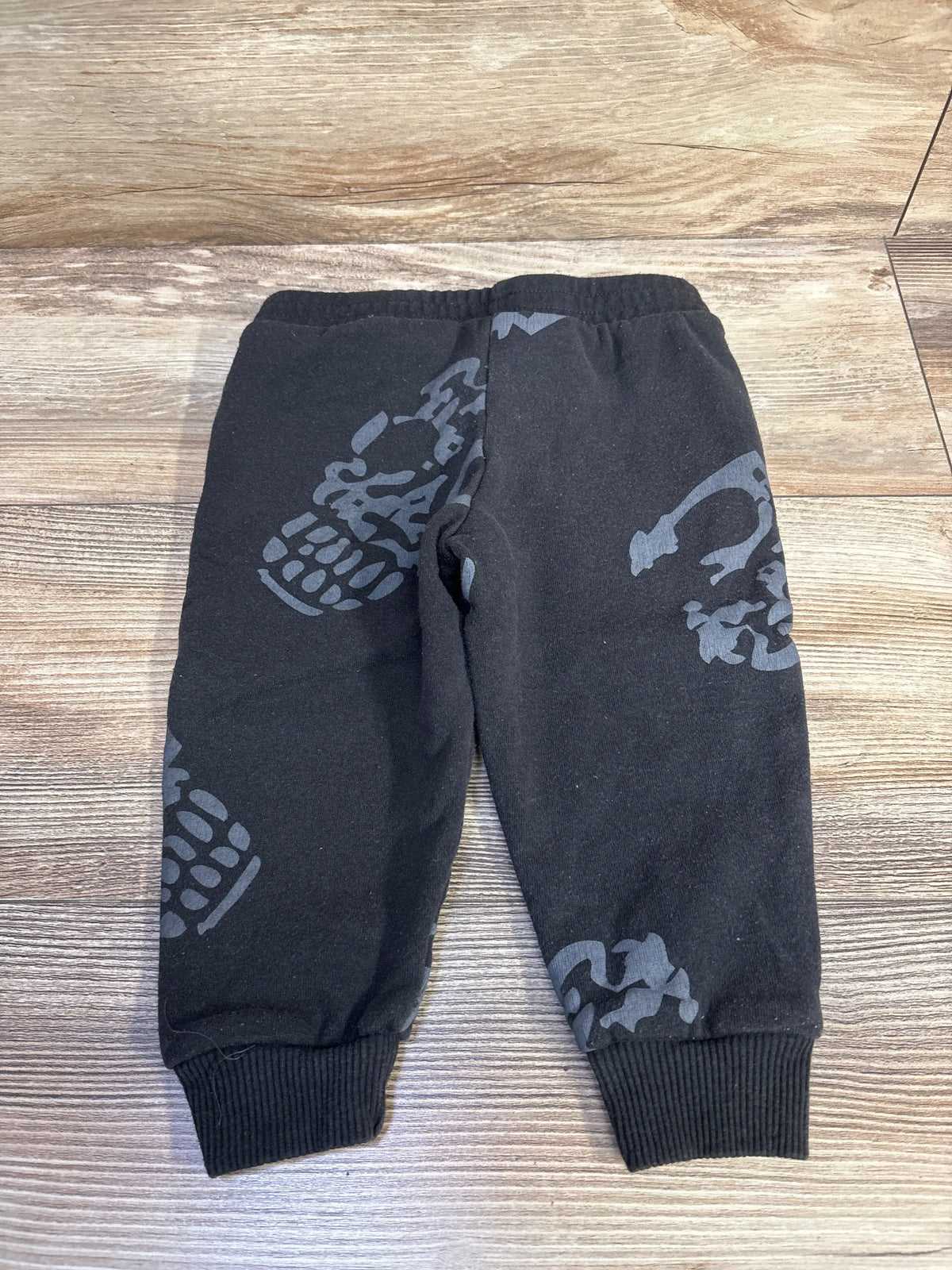 Front view of black Beetlejuice pull-on joggers, size 18 months, with gray graphics and ribbed cuffs on a wood floor