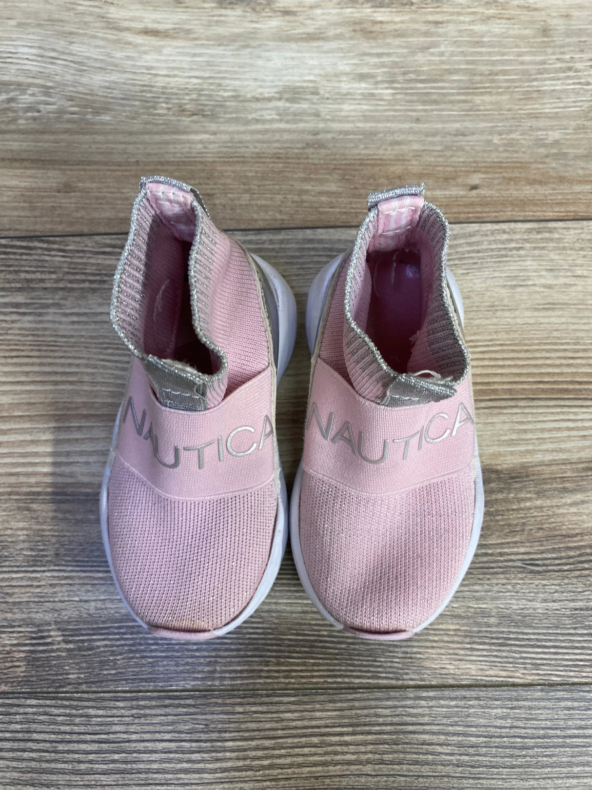 Top view of Nautica slip-on sneakers showing pink knit upper, NAUTICA elastic strap and glitter pull tab on wood floor