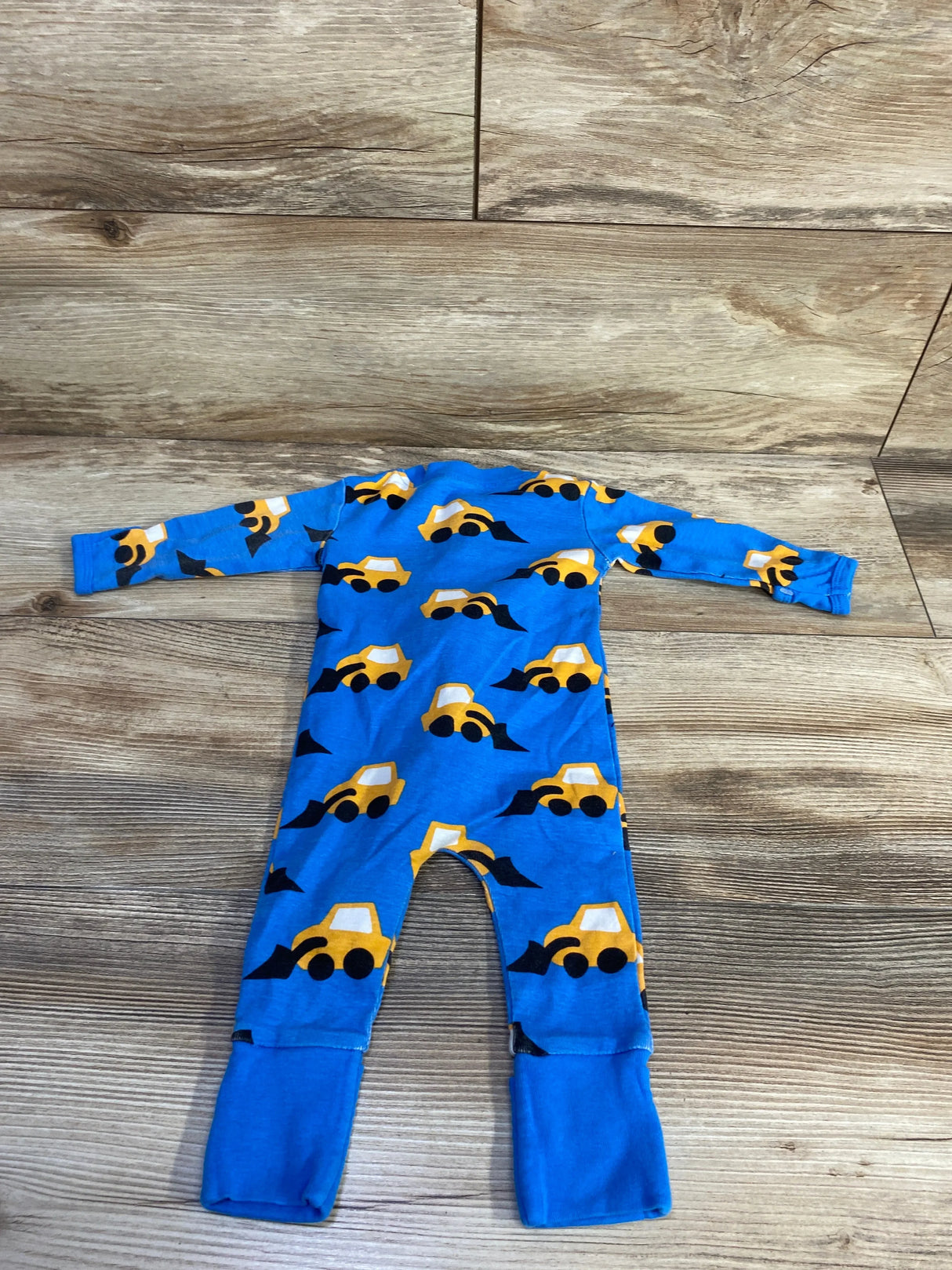 Flat lay of blue convertible sleeper with yellow construction truck print showcasing fold-over footies on wood background