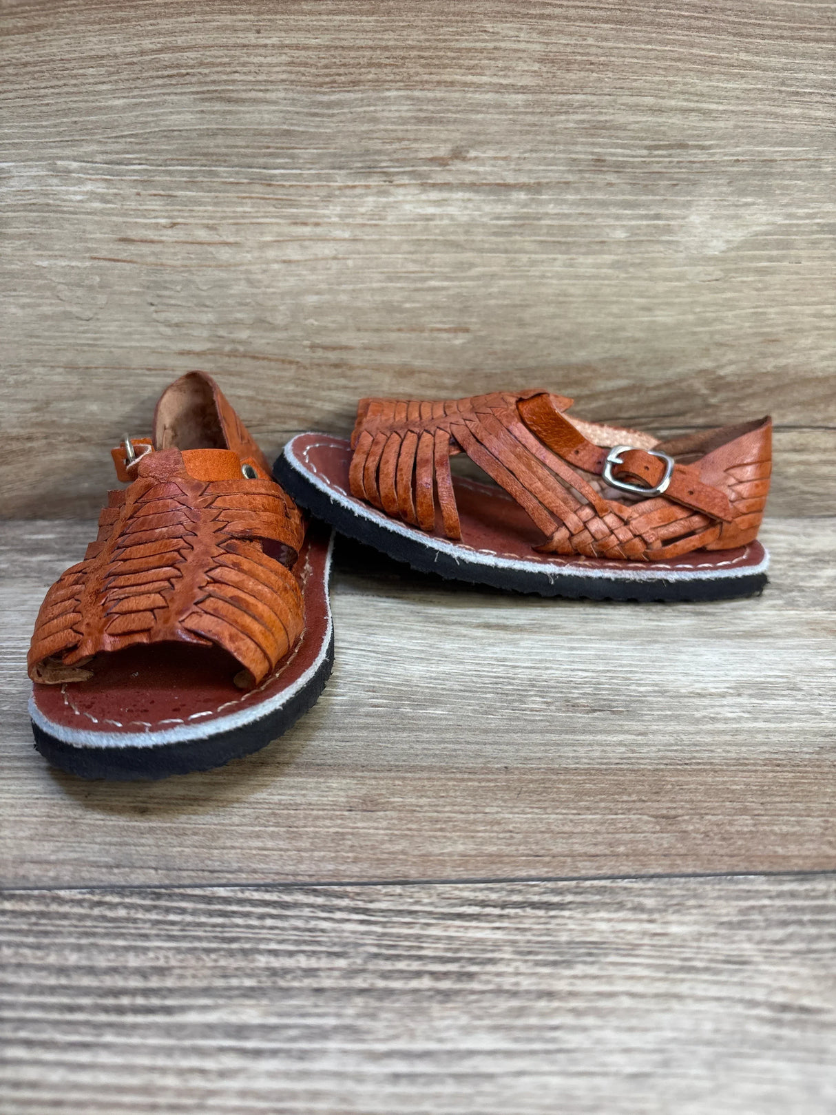 Brown leather kids huarache sandals with buckle on wooden background