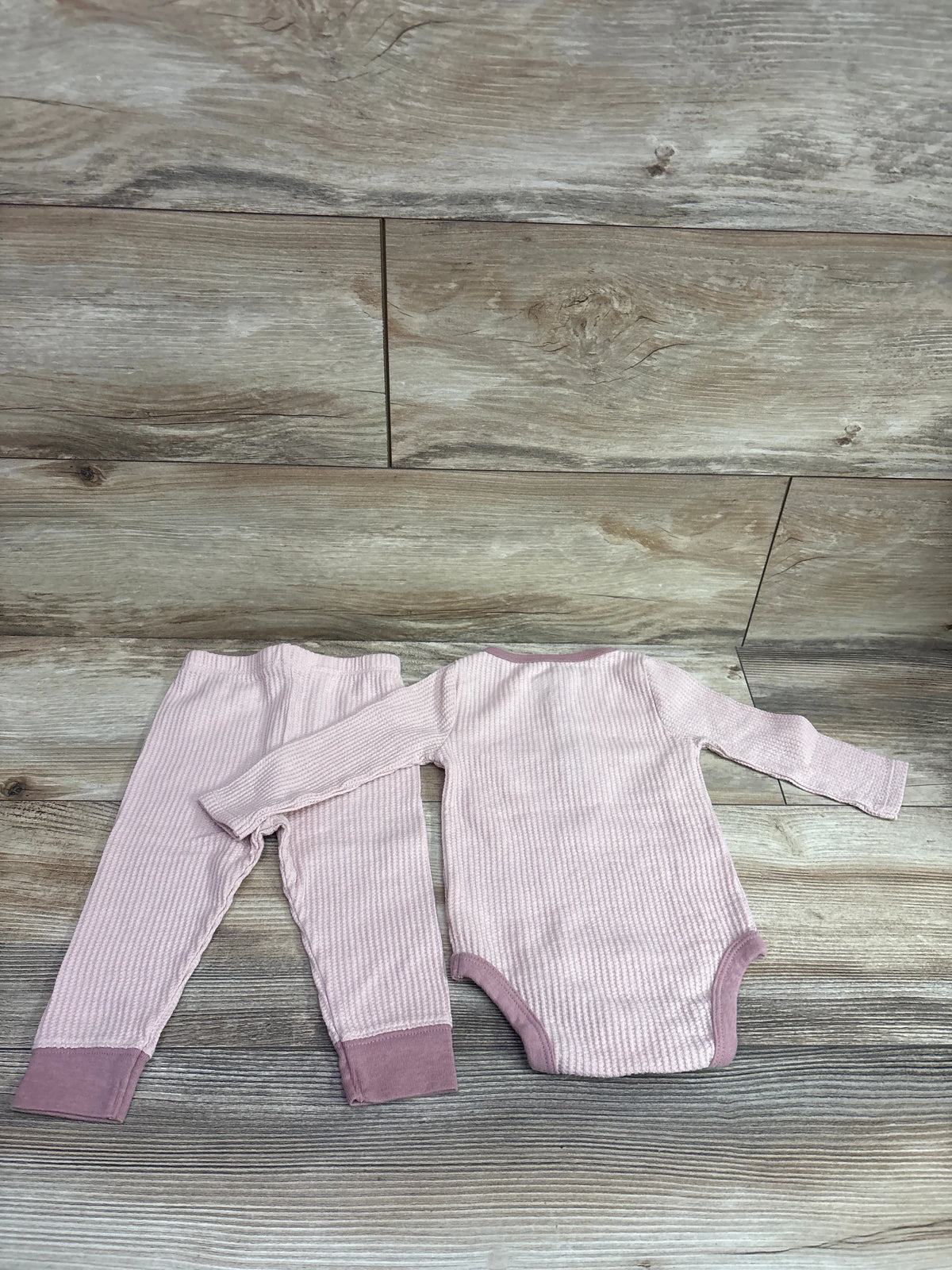 Top view of Cloud Island pink textured henley bodysuit and pants set for 6 to 9 months showcasing ribbed fabric on a wood surface
