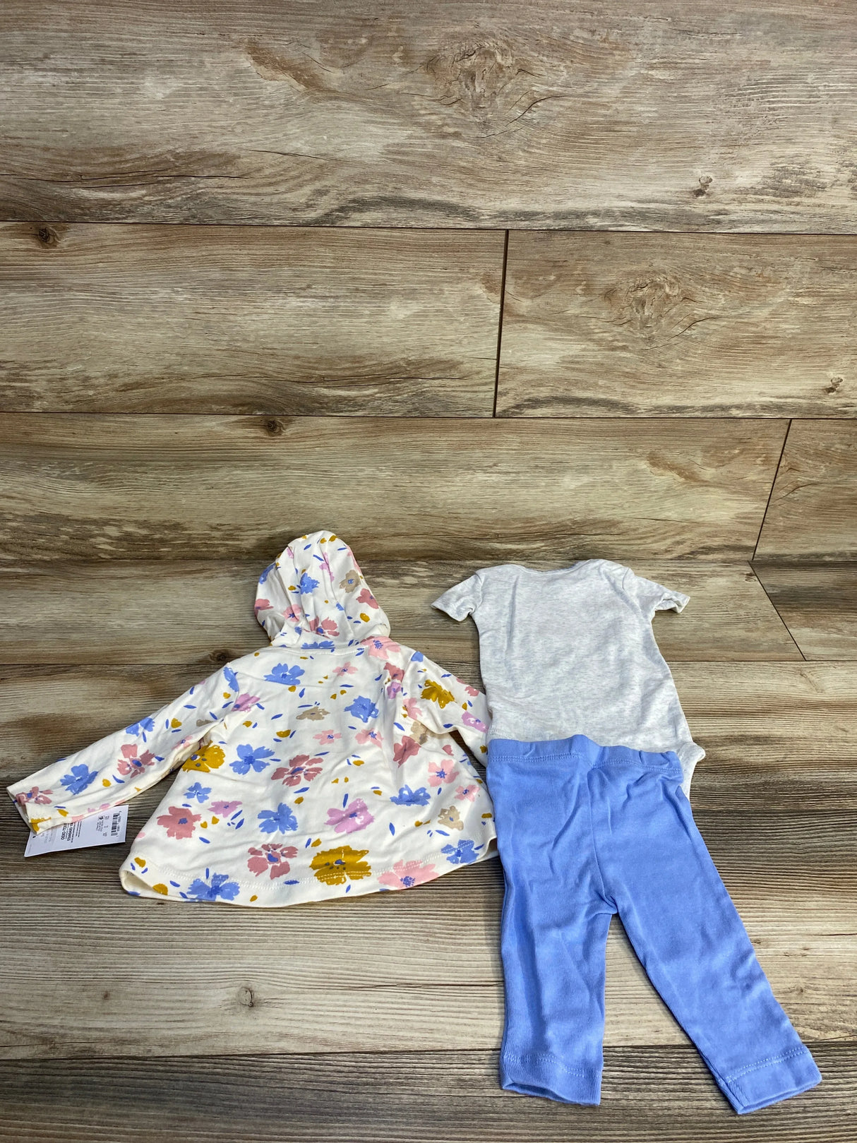 Baby girl outfit with floral hooded jacket, grey onesie, and blue leggings on wood background