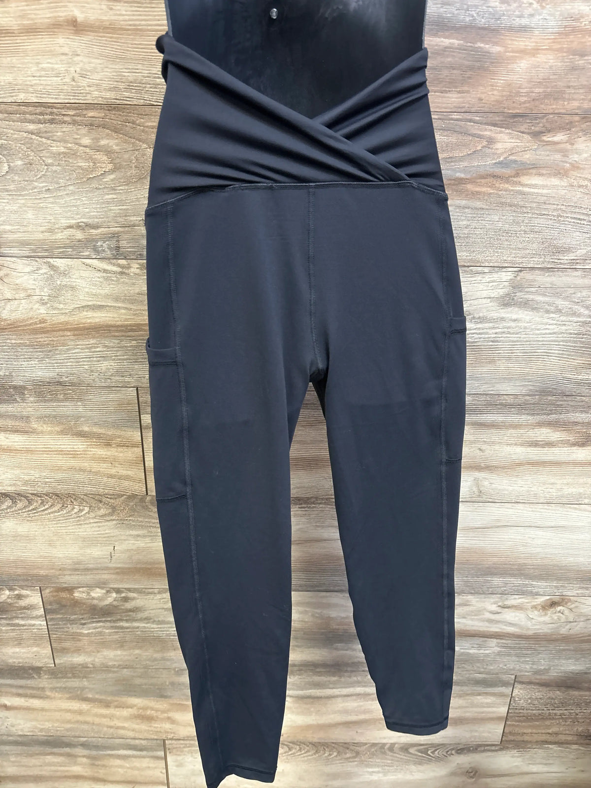 Front view of Isabel maternity active leggings in black with crossover waistband and side pockets on wood flooring
