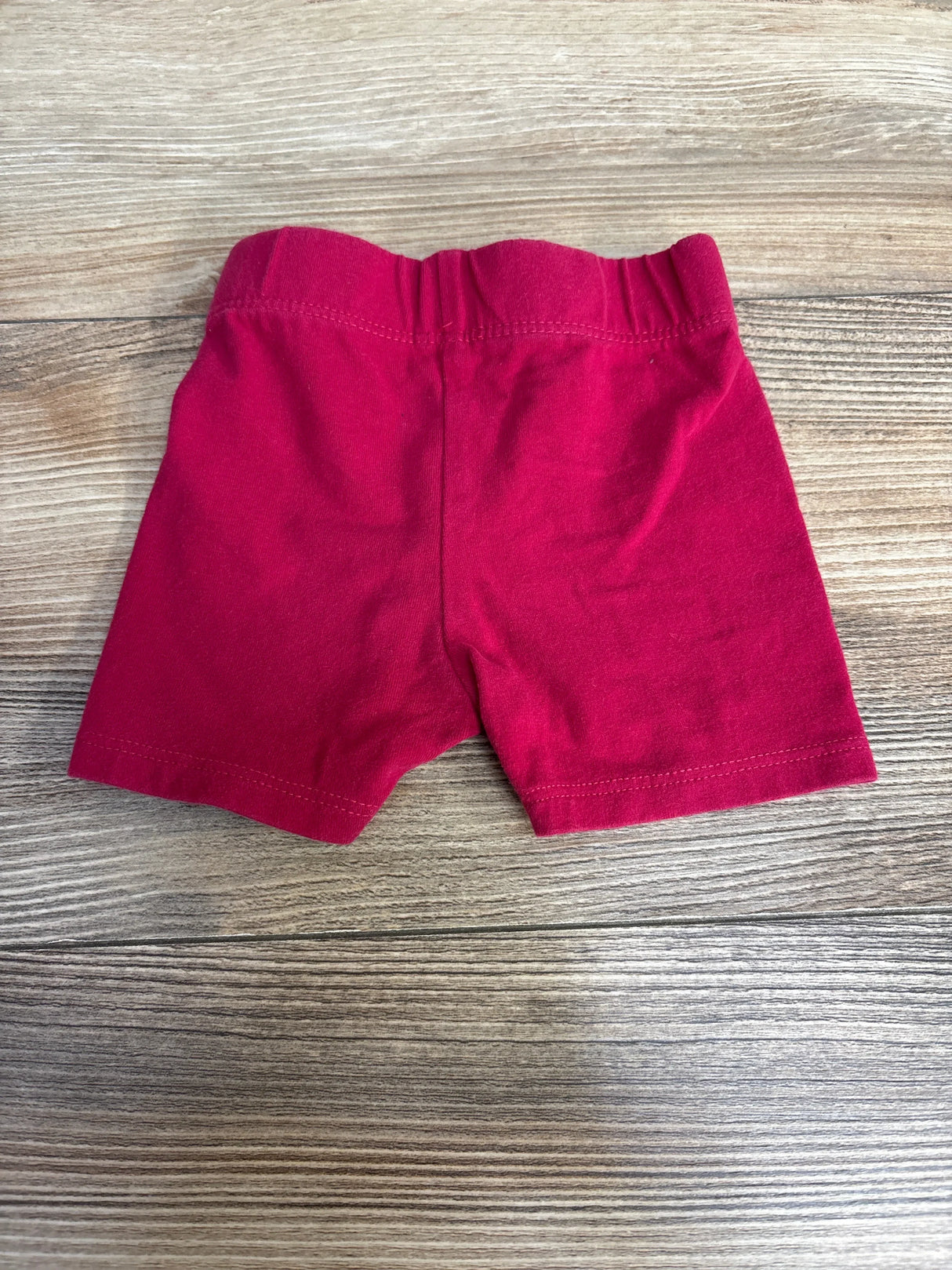 Back view of pink baby bike shorts (3-6 months) showcasing elastic waistband and knit fabric on a light wood background