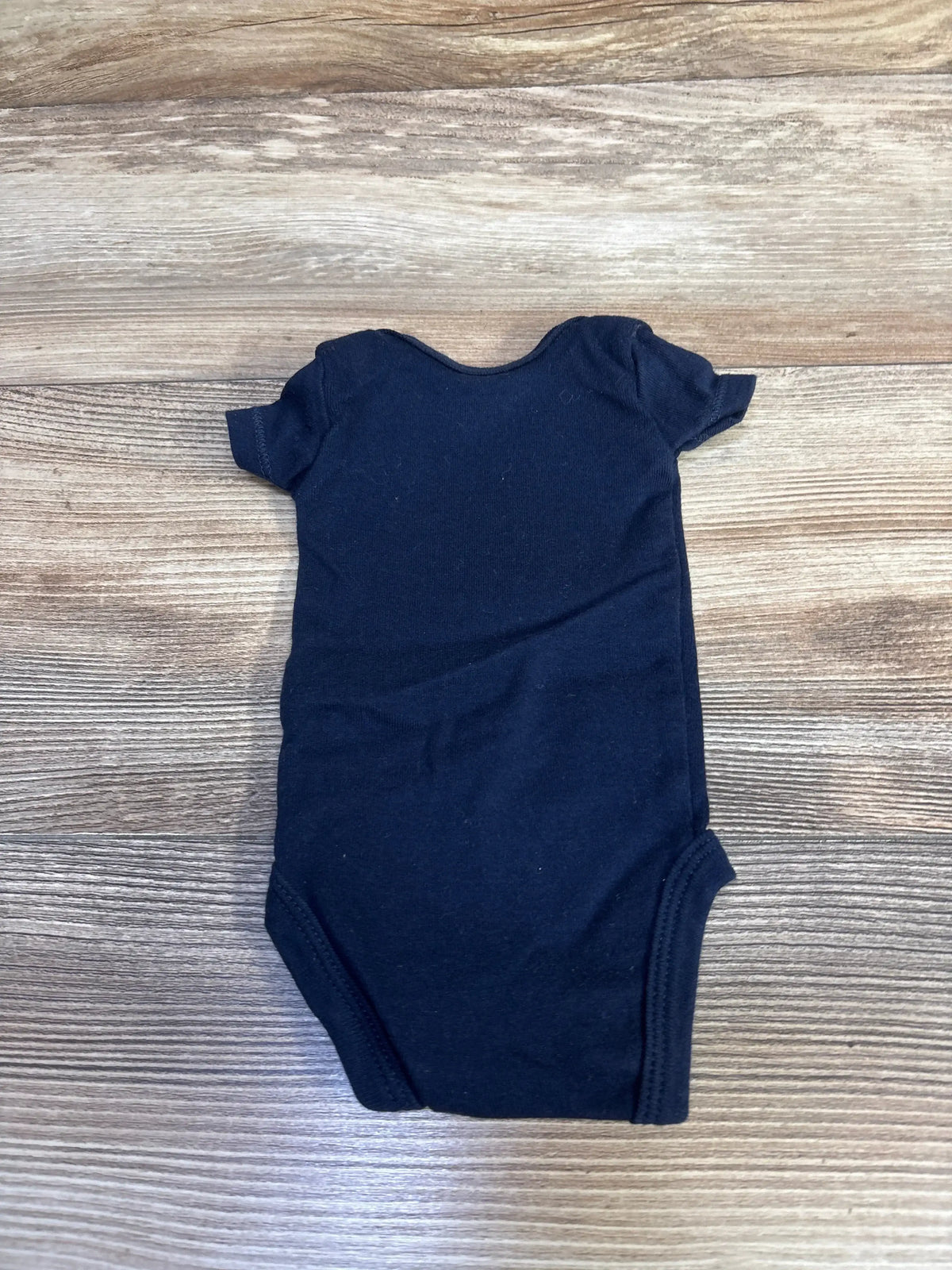 Flat-lay back of preemie Carter’s navy bodysuit showing short sleeves, elastic leg openings, and plain back on wood background
