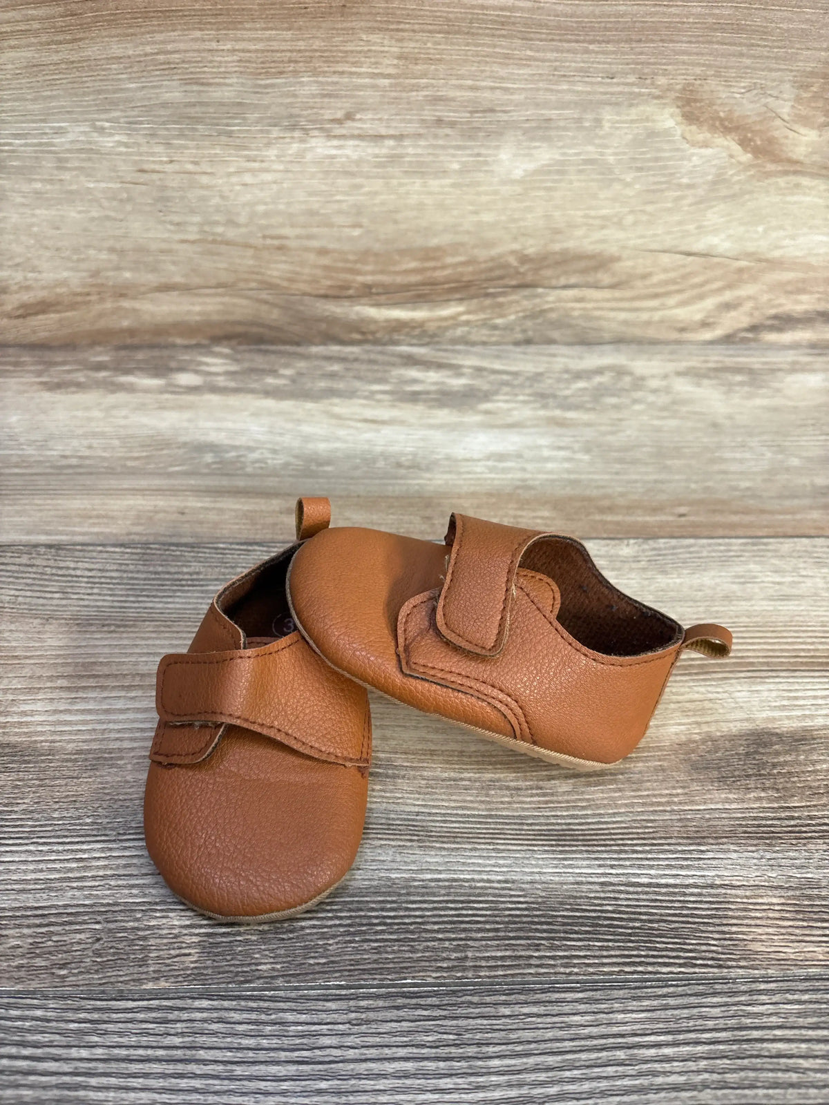 Top and side view of brown Baywell faux leather first walking soft sole shoes showing hook and loop closures and pull tabs