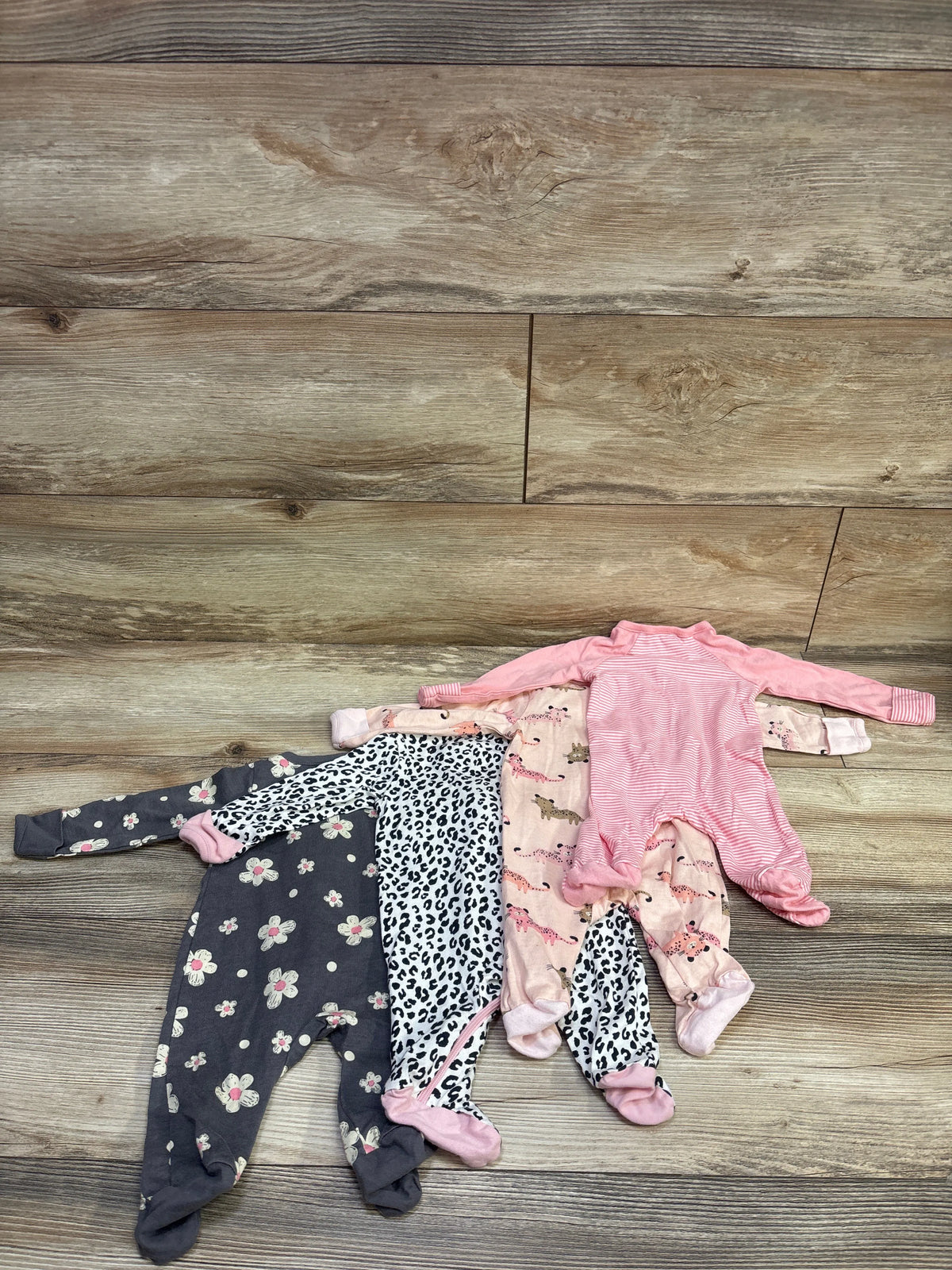 Top view of four Gerber Sleep N Play sleepers in pink newborn size showcasing striped, floral, leopard, and animal prints on wood