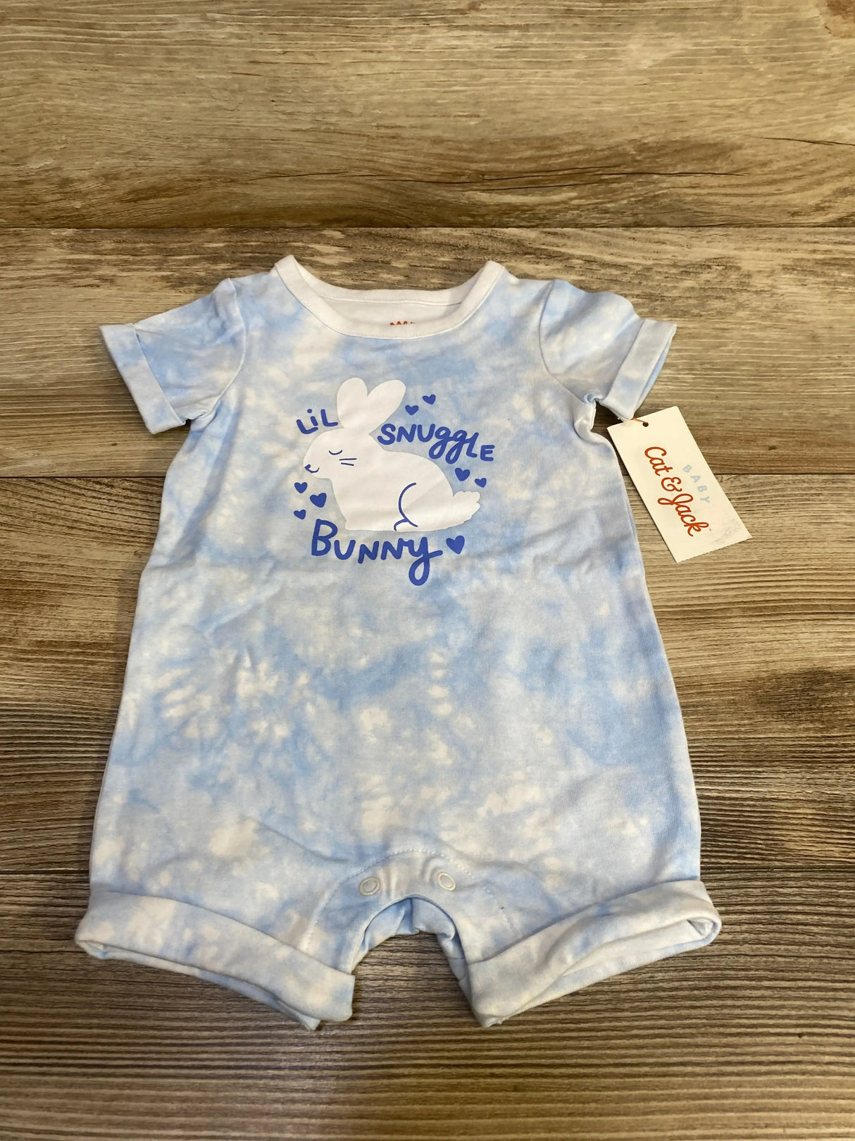 Flat lay of Cat and Jack Lil Snuggle Bunny blue romper with bunny graphic, short sleeves and snap crotch on wood floor